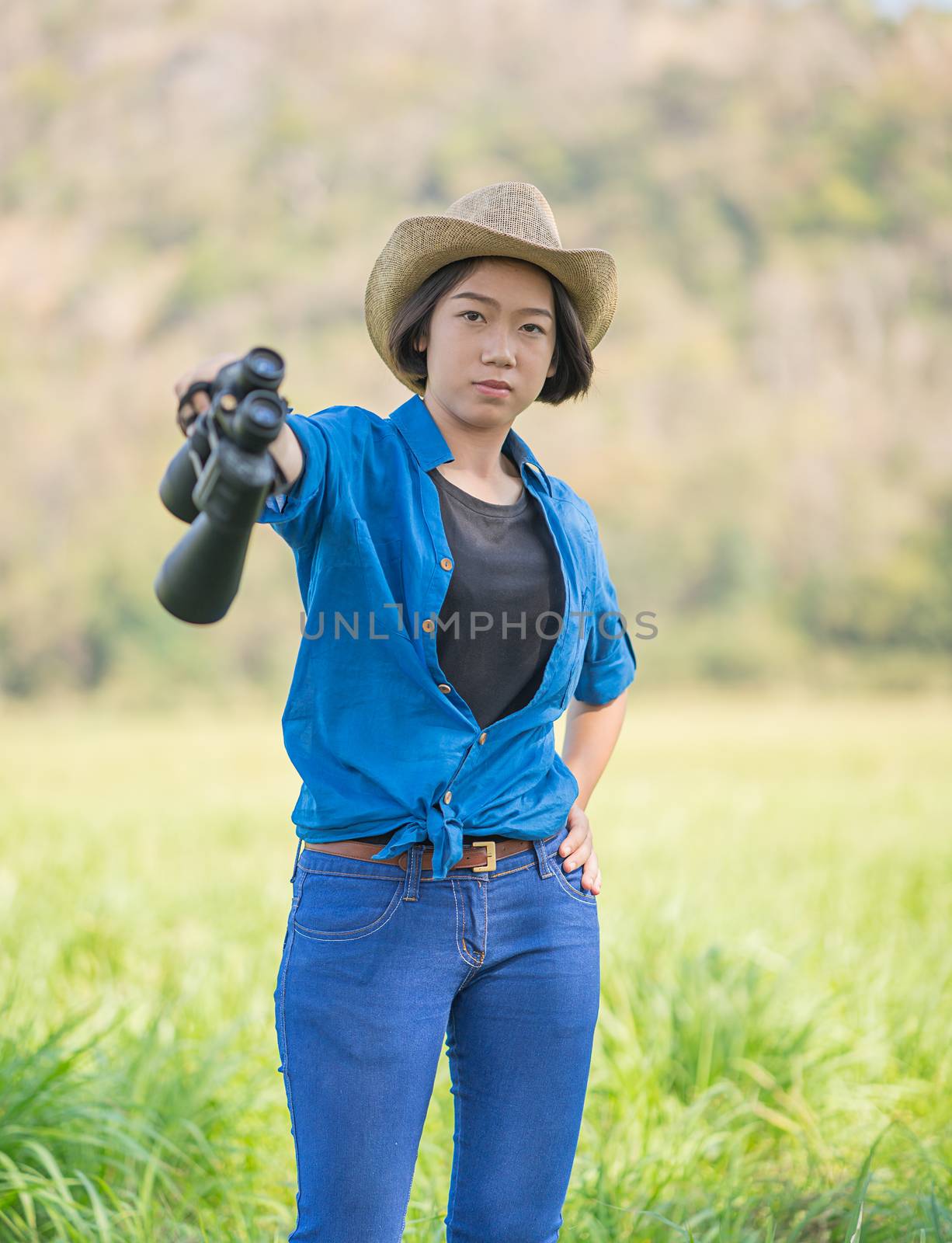 Young asian woman short hair wear hat and hold binocular in grass field countryside Thailand