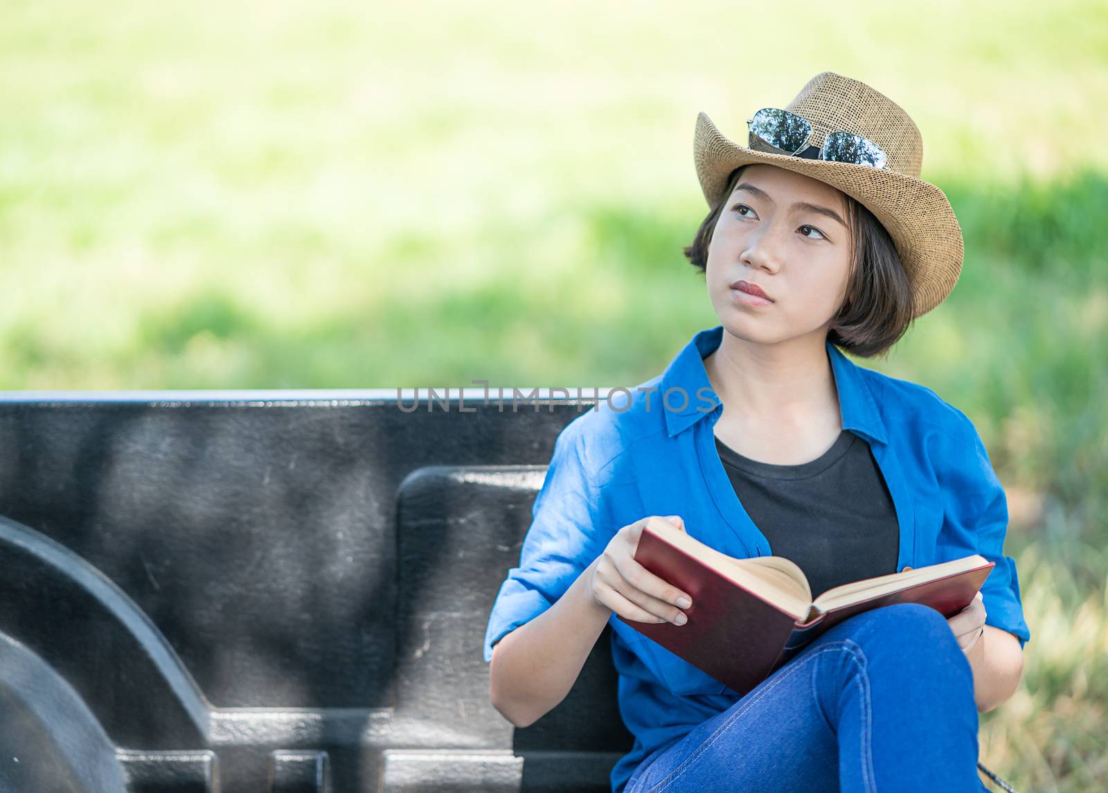 Young asian women short hair wear hat and sunglasses read a book ,sit on pickup truck in countryside Thailand