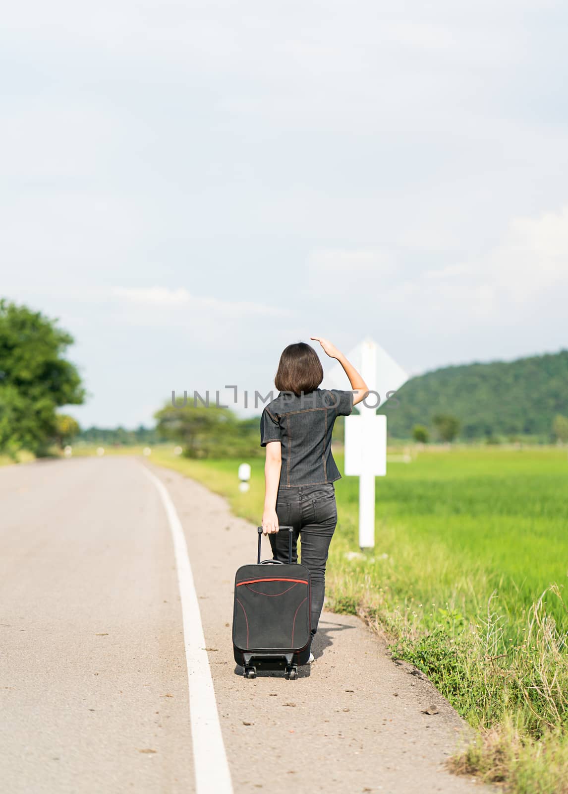 Woman with luggage hitchhiking along a road by stoonn