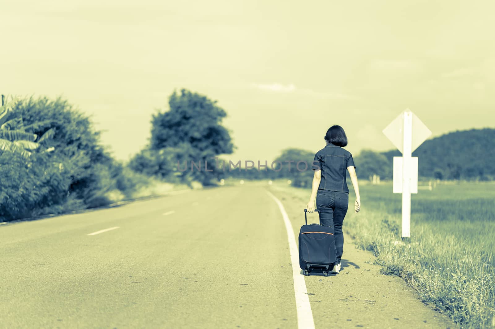 Woman with luggage hitchhiking along a road by stoonn