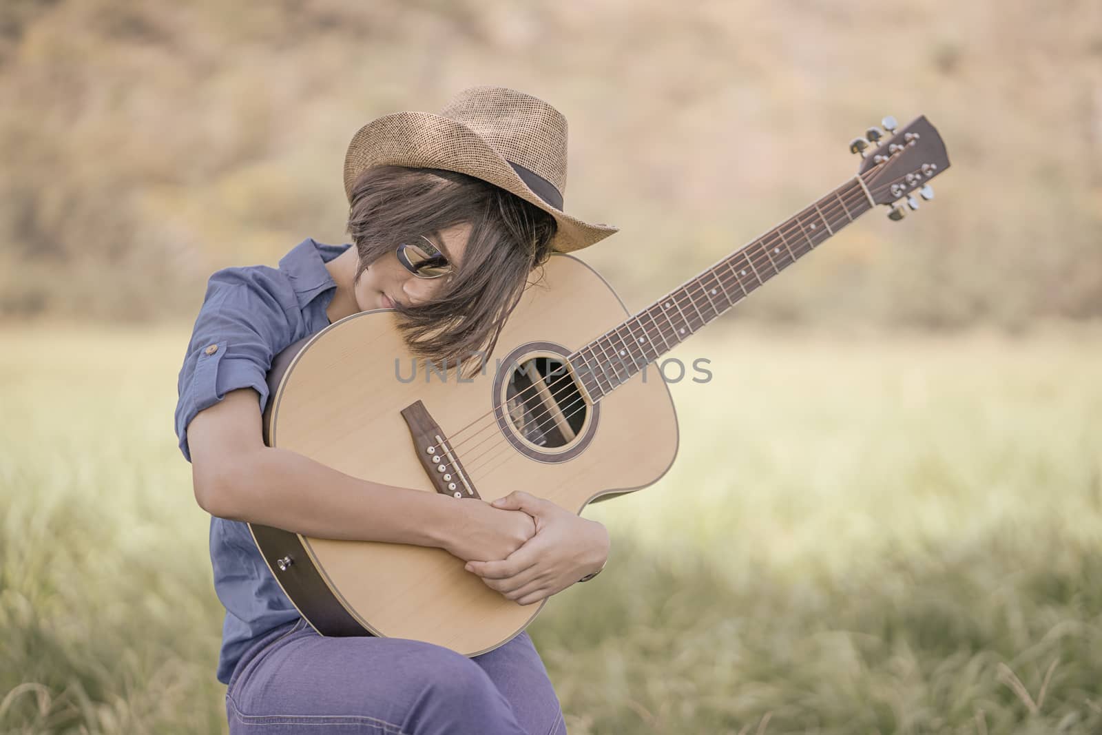 Young asian women short hair wear hat and sunglasses sit playing guitar in grass field countryside Thailand