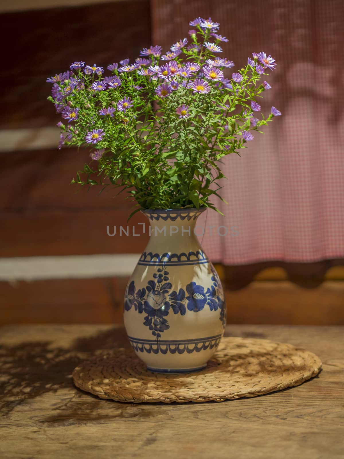 bunch of pink violet flowers in rustic ceramic painted vase on oak wood table in timbered cottage house
