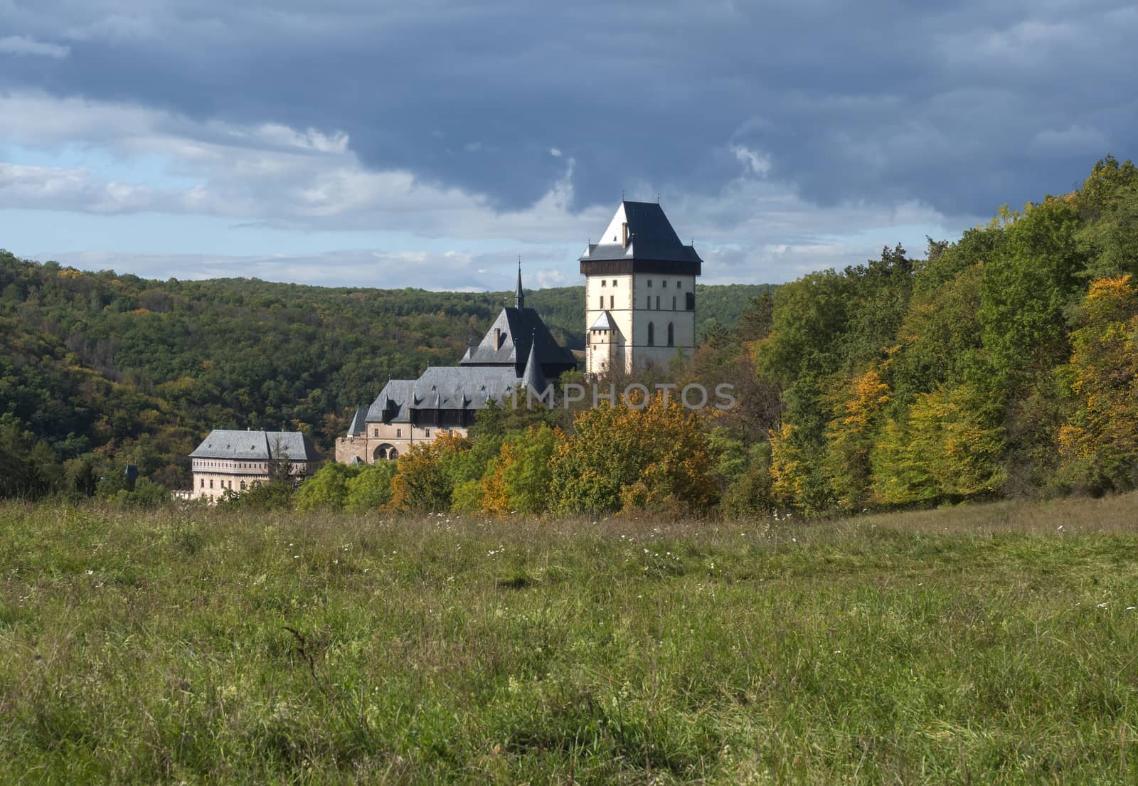 Karlstejn gothic state castle near Prague, the most famous castle in Czech Republic with grass meadow and autumn colored trees and forest. Blue sky clouds background. Located near Prague..
