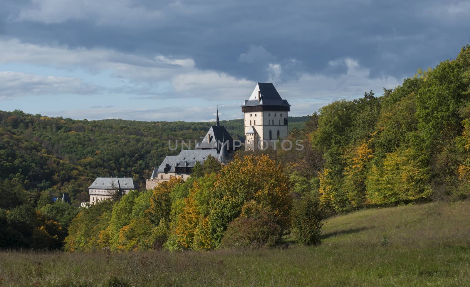 Karlstejn gothic state castle near Prague, the most famous castle in Czech Republic with grass meadow and autumn colored trees and forest. Blue sky clouds background. Located near Prague. by Henkeova