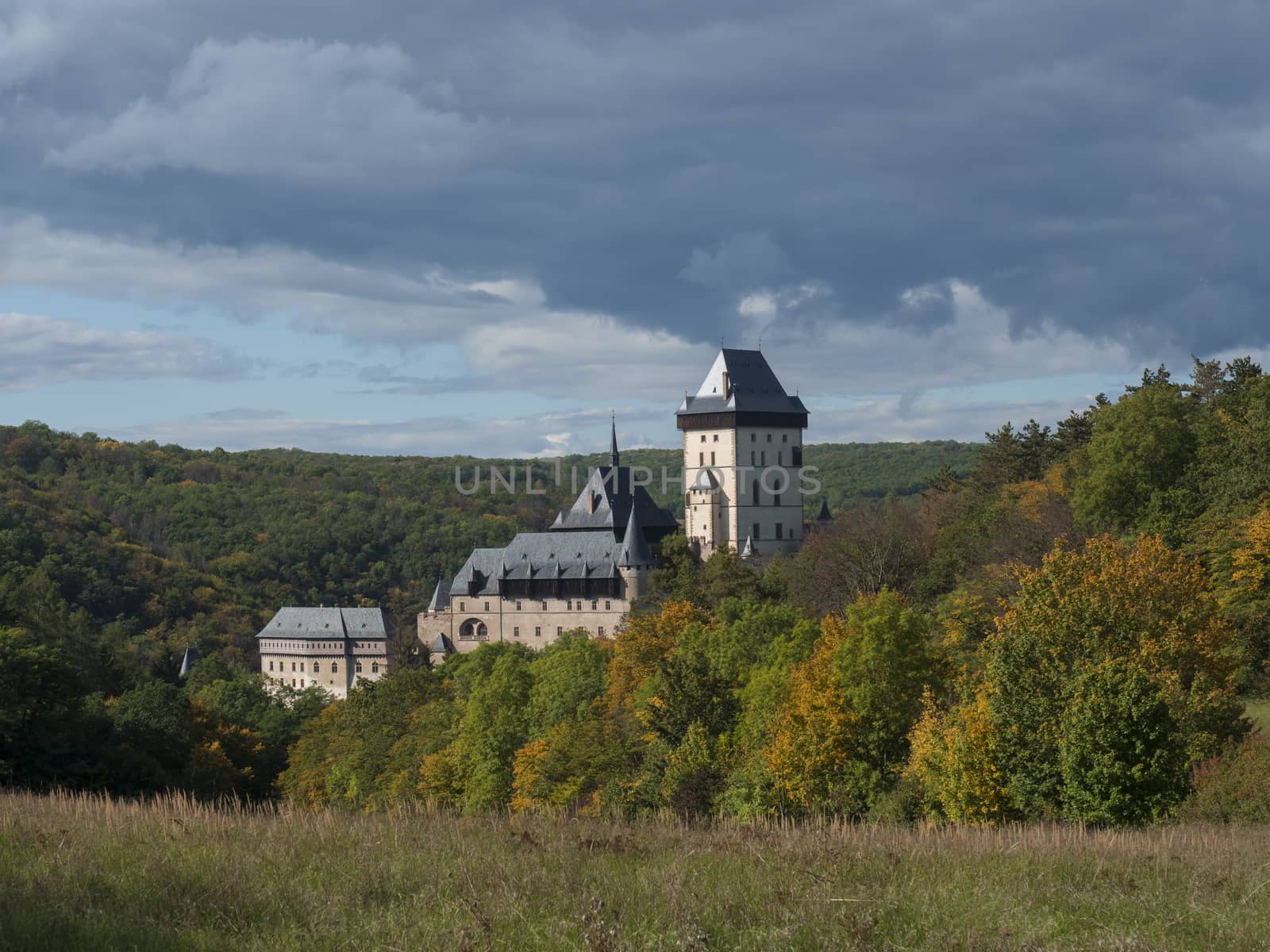 Karlstejn gothic state castle near Prague, the most famous castle in Czech Republic with grass meadow and autumn colored trees and forest. Blue sky clouds background. Located near Prague..