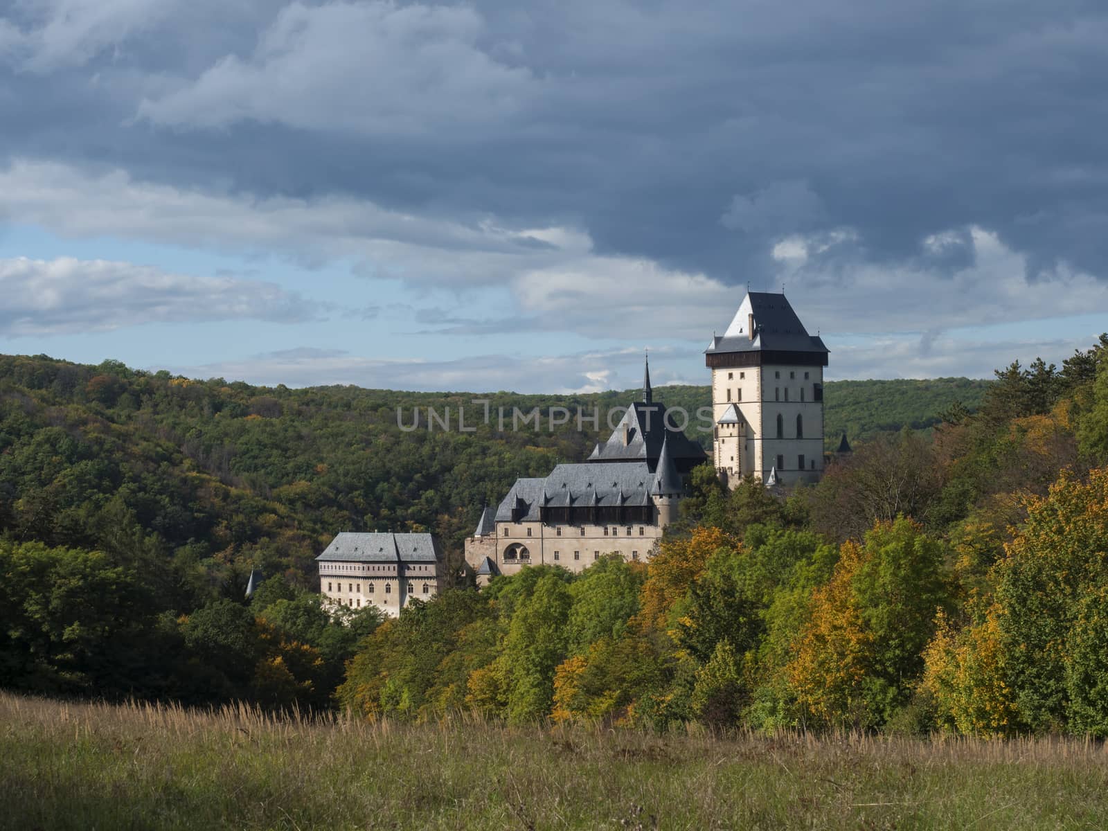 Karlstejn gothic state castle near Prague, the most famous castle in Czech Republic with grass meadow and autumn colored trees and forest. Blue sky clouds background. Located near Prague. by Henkeova