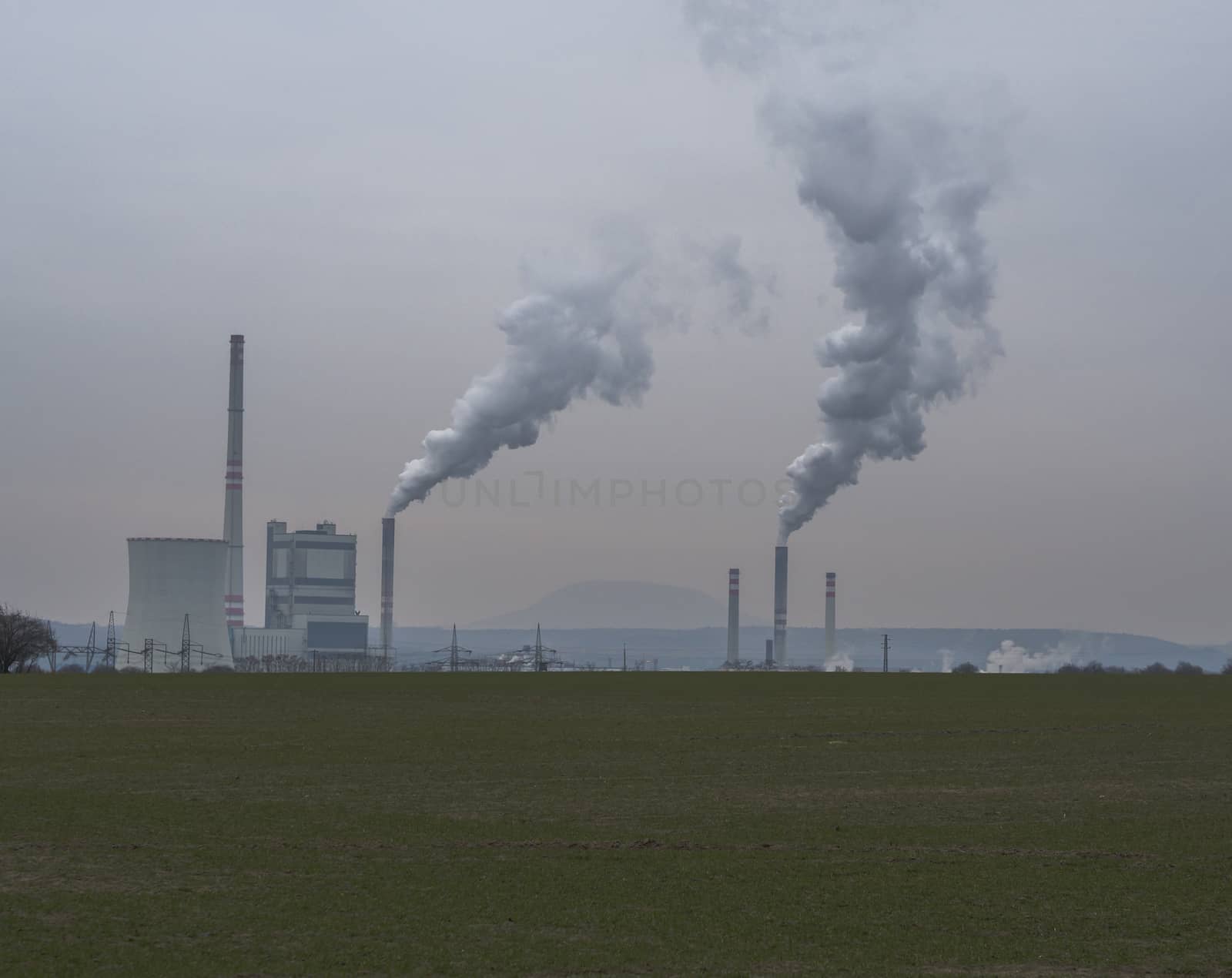 thermal power station with smoking chimney in winter evening green grass foreground