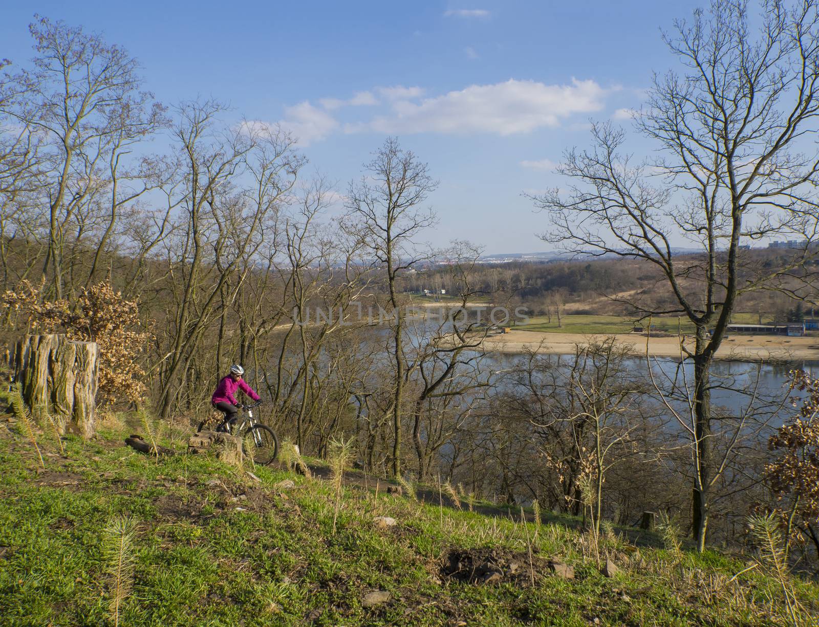 Czech republic, Prague, Hostivarska prehrada, April 2, 2018: women in pink riding the bike around artificial lake dam on early spring sunny day, tree and blue sky background