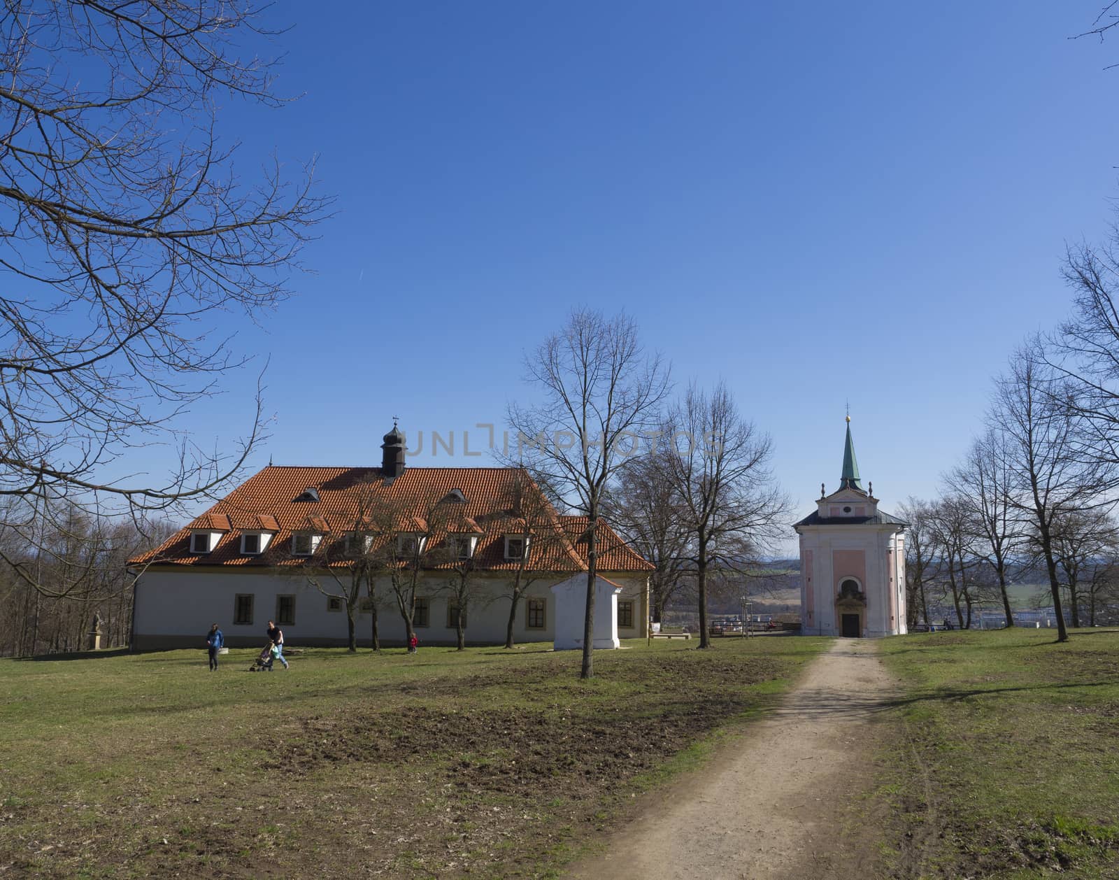 Czech Republic, Skalka, April 7, 2018: baroque monastery Skalka with small chapel in sunny day early spring, grass, bare tree and blue sky background