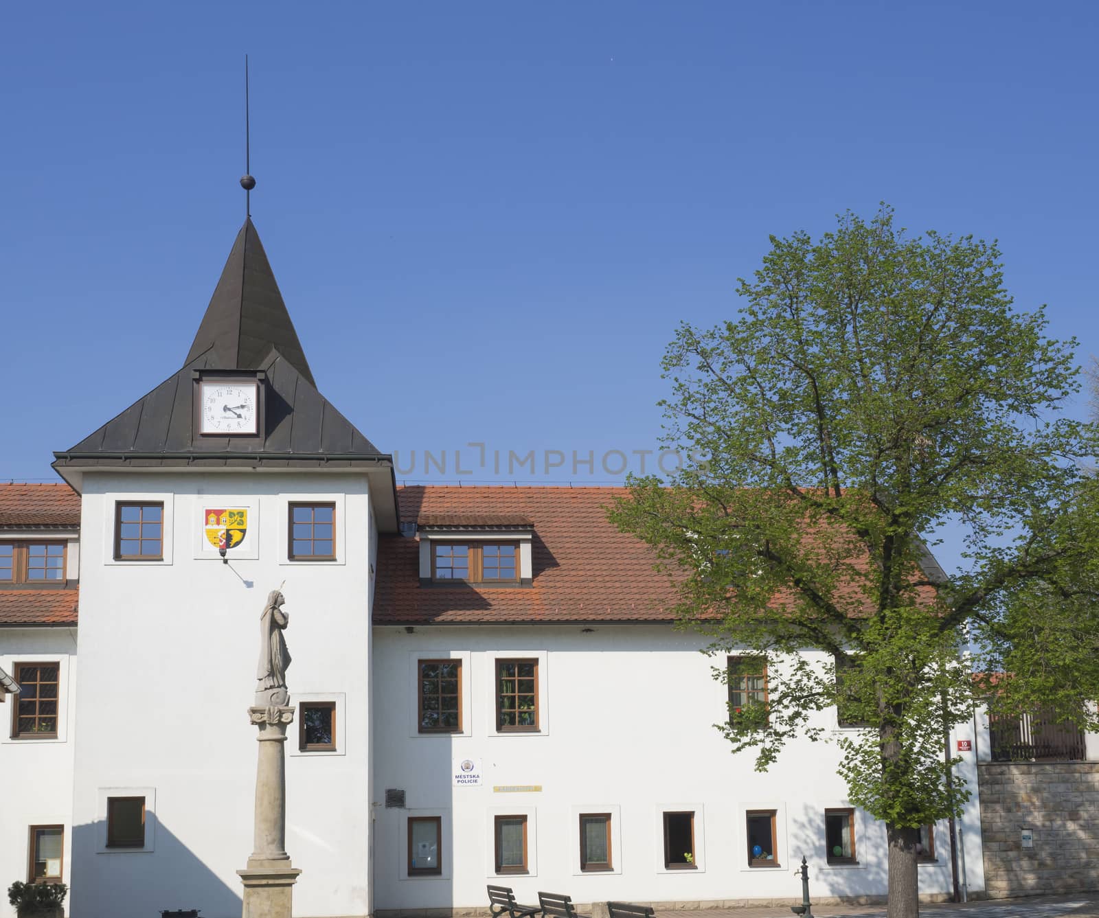 Czech Republic, Prague, Dolni Pocernice, April 21, 2018: old village Town hall with tower clock and stone staue,  green tree and blue sky background