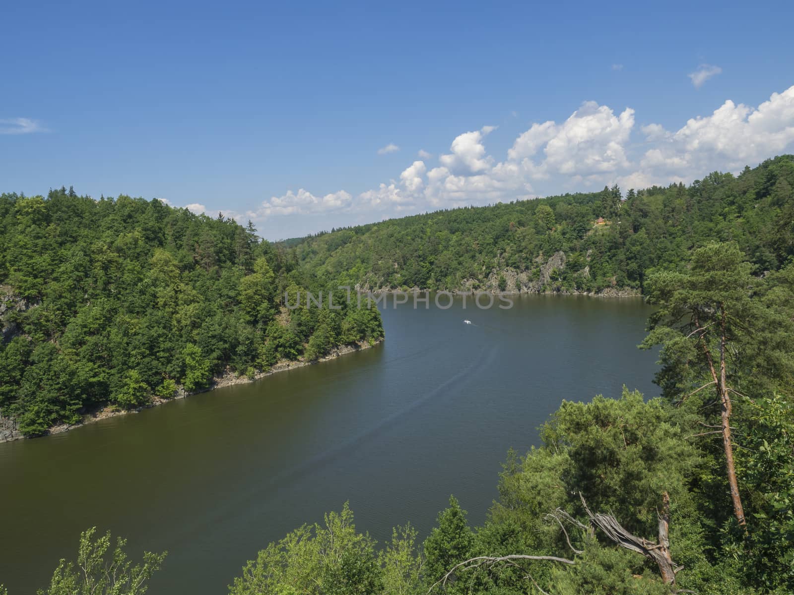 view from bridge zvikov on otava and vltava river with green tree forest rocky shore blue water, boat and blue sky white clouds background