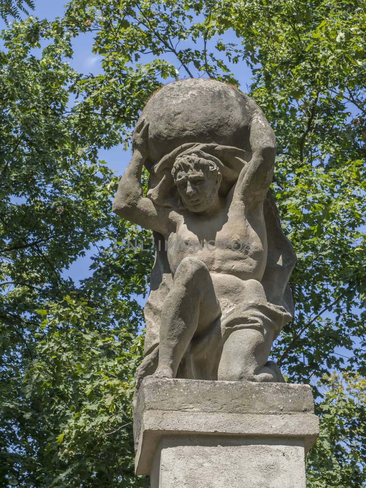 Stone men figure carrying stone, baroque statue from Greek mythology of Sisyphus or Sisyphos, garden, green trees background, czech republic