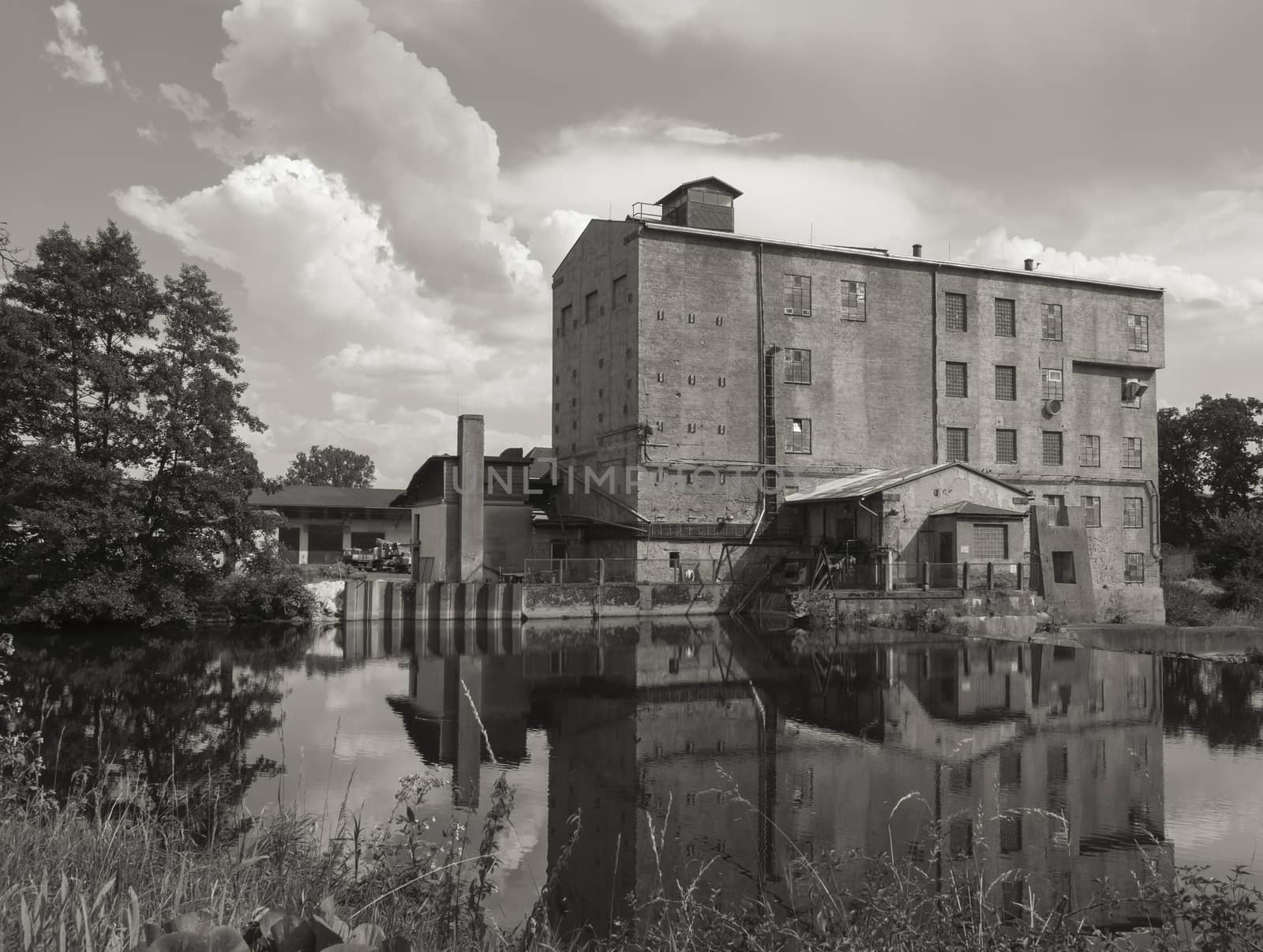 View accros Jizera river on abandoned, aged, dirty, empty industrial factory building in sepia tone toned, dramatic clouds and tree