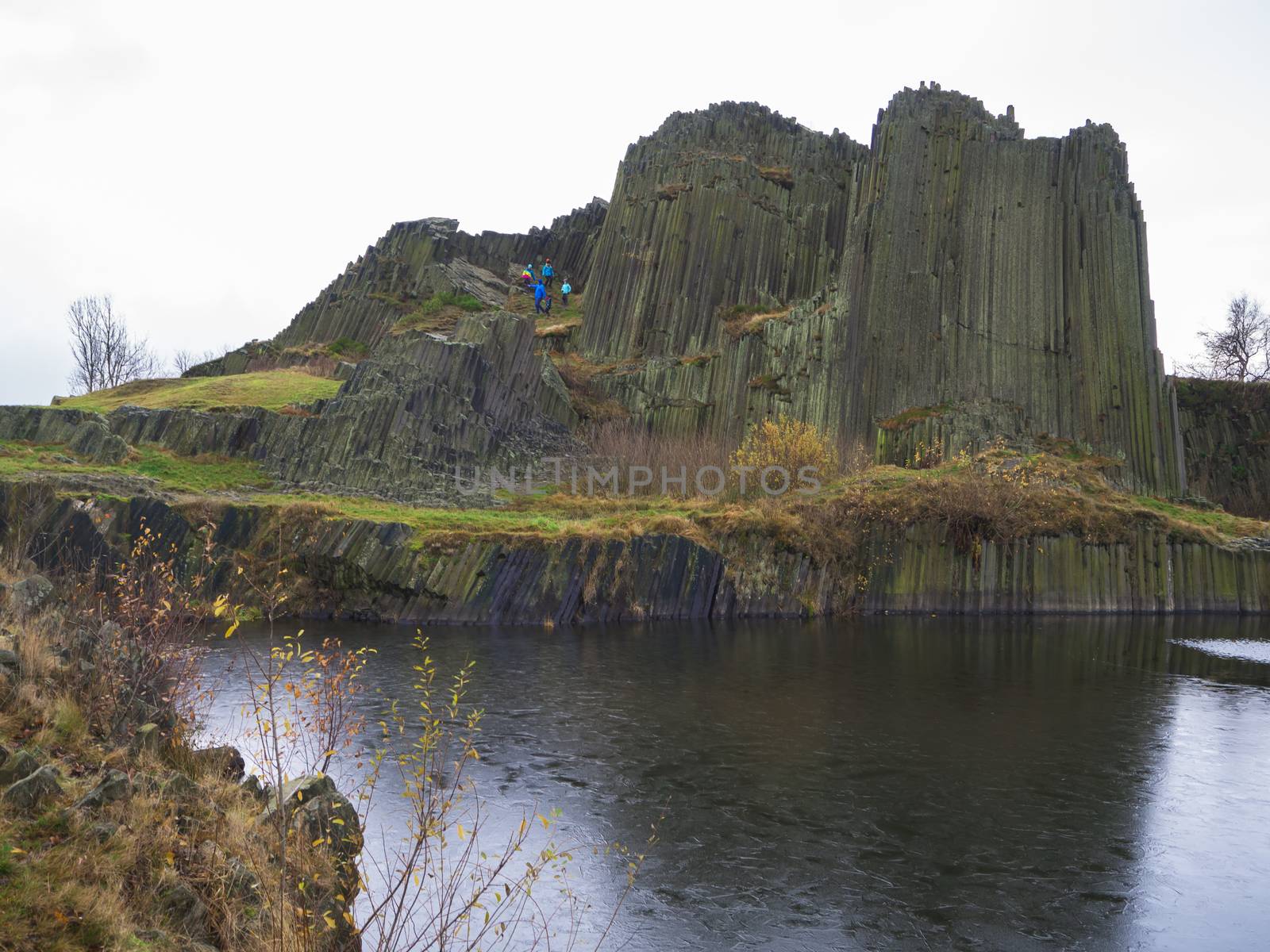 basalt pillars lava vulcanic rock formation organ shape with lake panska skala and group of tourist in blue jacket in kamenicky senov prachen czech republic