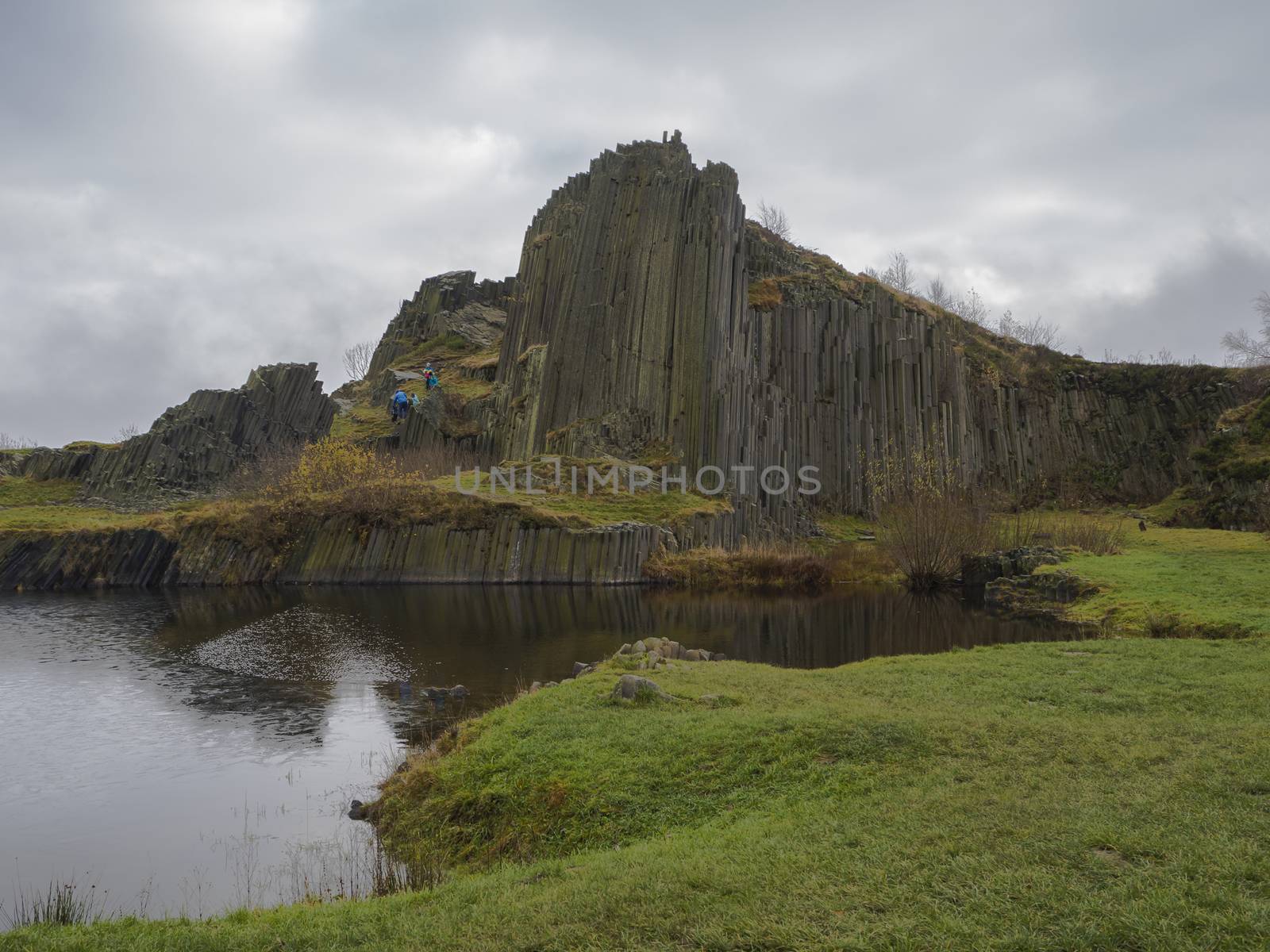 basalt column pillars lava vulcanic rock formation organ shape with lake panska skala and group of tourist in blue jacket in kamenicky senov prachen czech republic