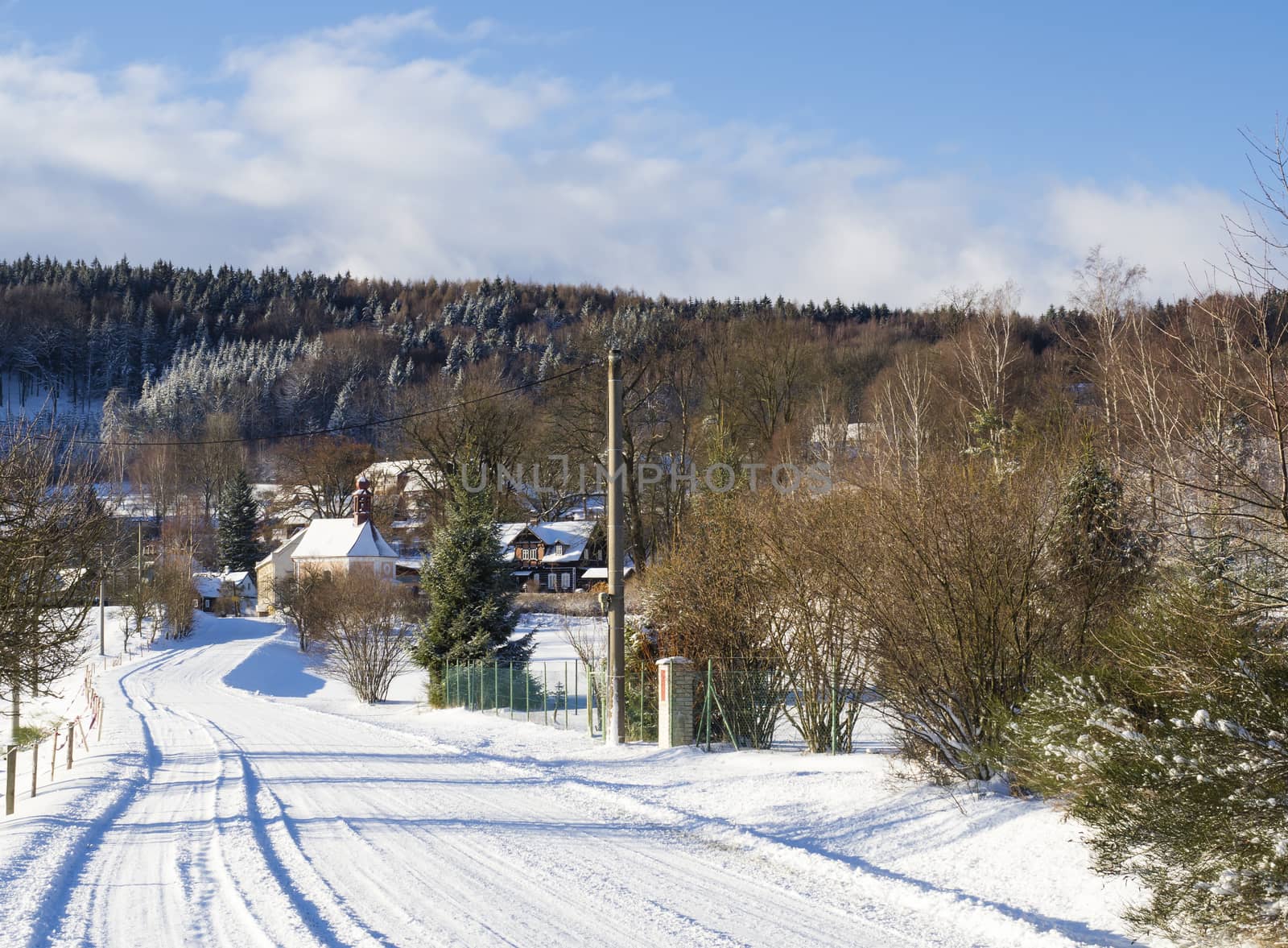 winter view on village travnik with chapel, timbered cottage and trees, snow covered rural landscape with in luzicke hory mountain, sunny day.