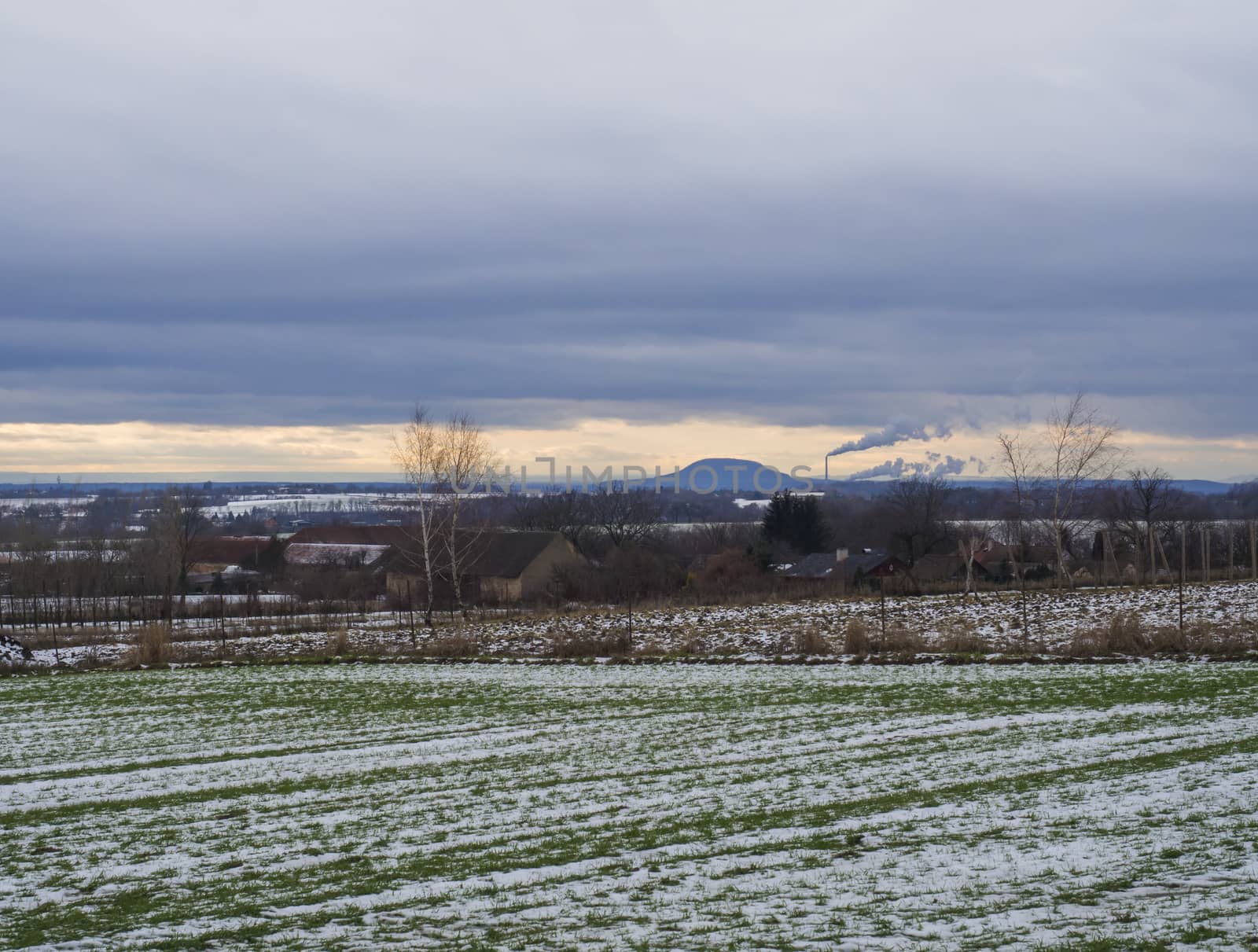 Winter rural landscape with green snow covered fields at sunset. View of the mountain Rip hill with smoking chimney, popular pilgrimage place, central Bohemian region. Czech Republic