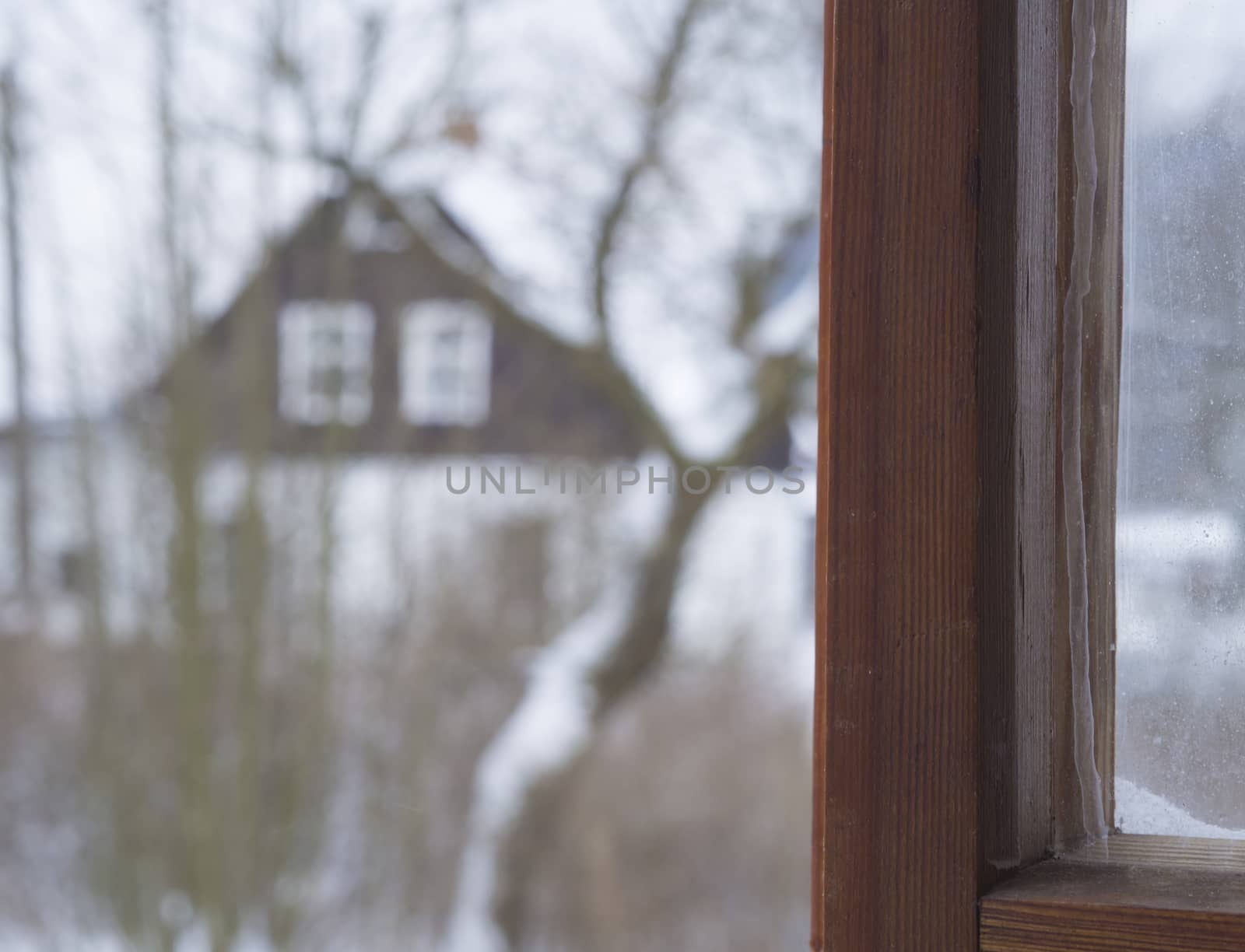 view from wooden window on blurred winter rural landscape snow covered trees a and timbered cottage - selective front focus