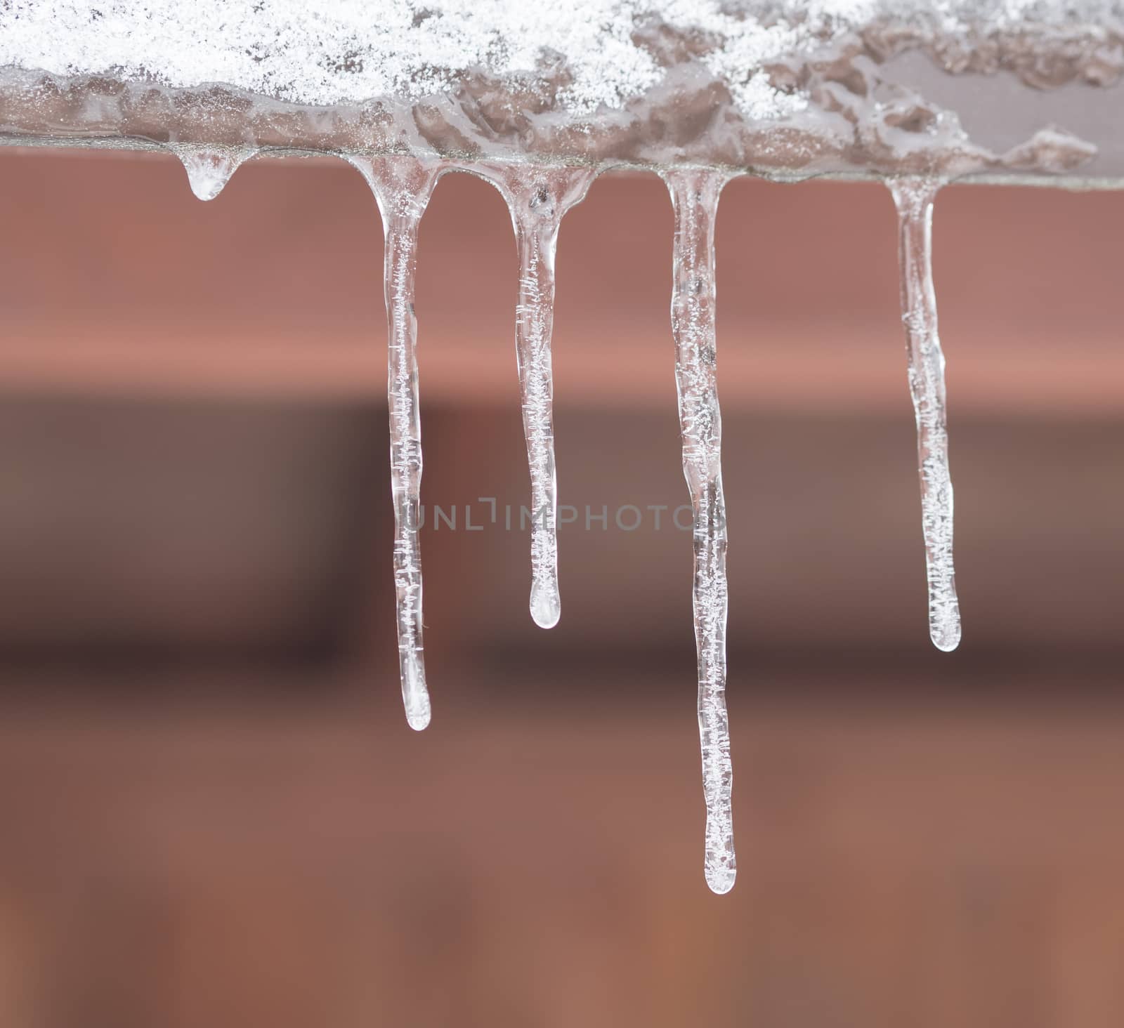 close up icicles hanging down from the tin roof, selective focus,orange winter frozen background