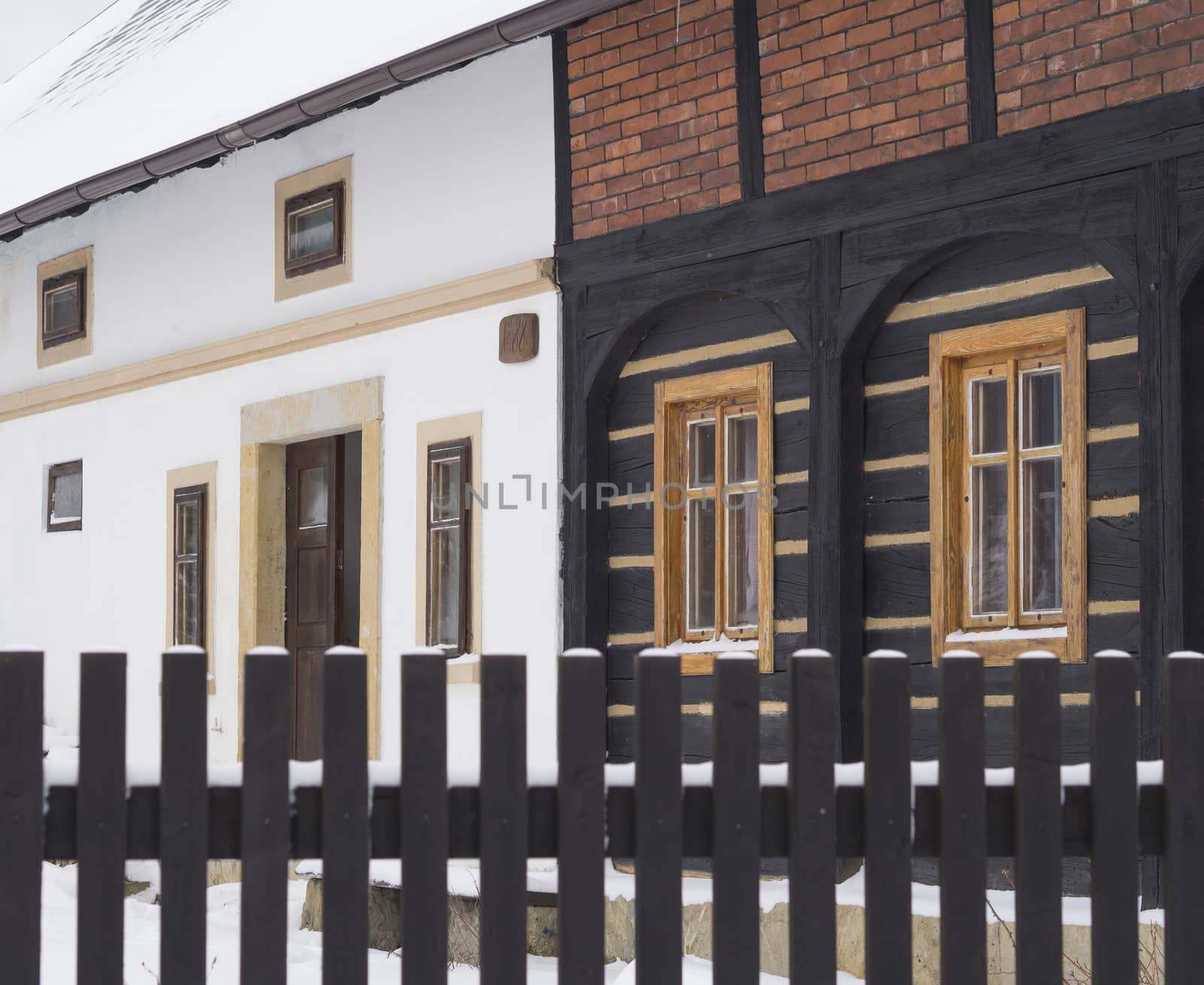 view from wooden plank fence on  timbered cottage open front door in winter and snow