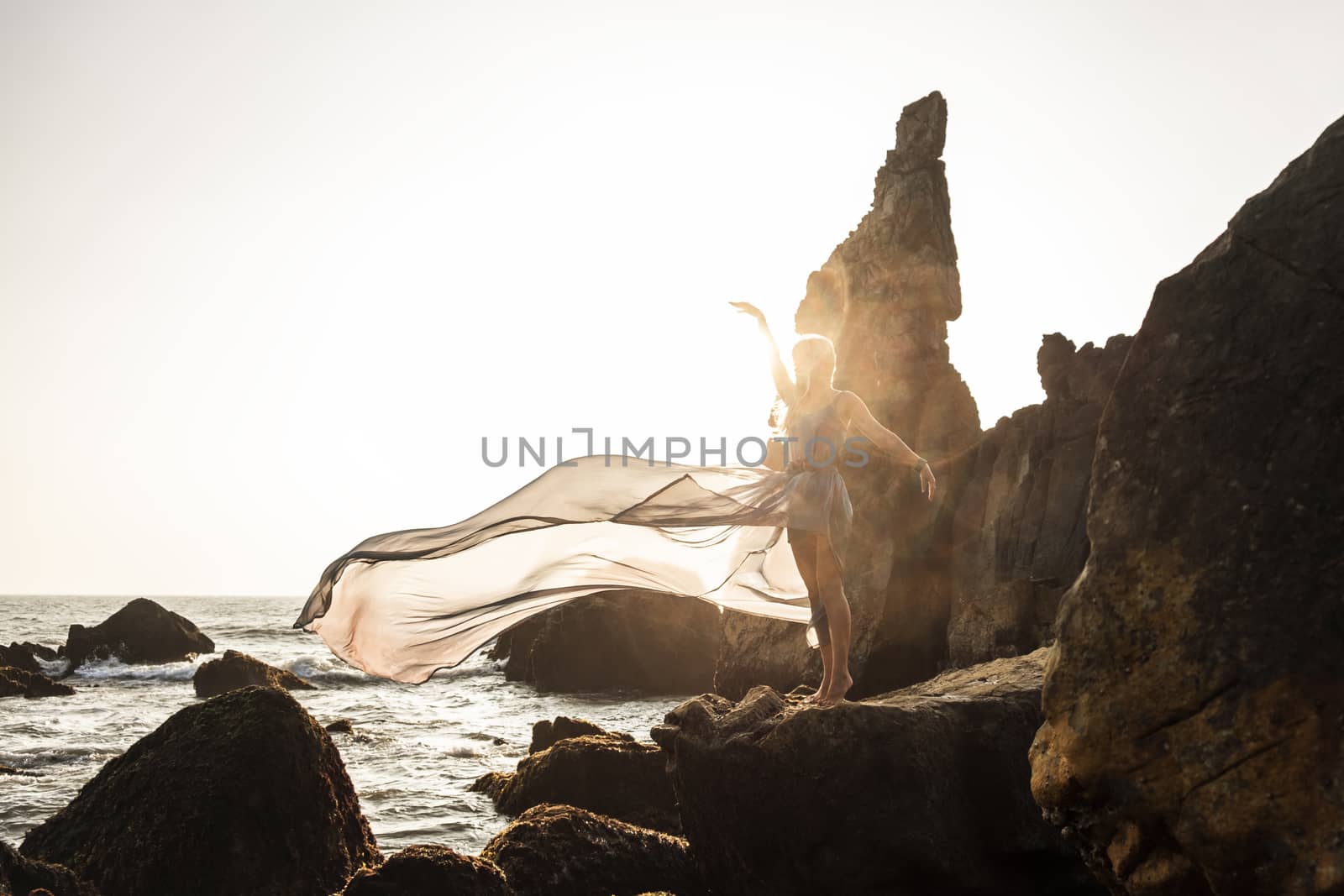 Beautiful European girl in a long dress stands on the rocks by the sea