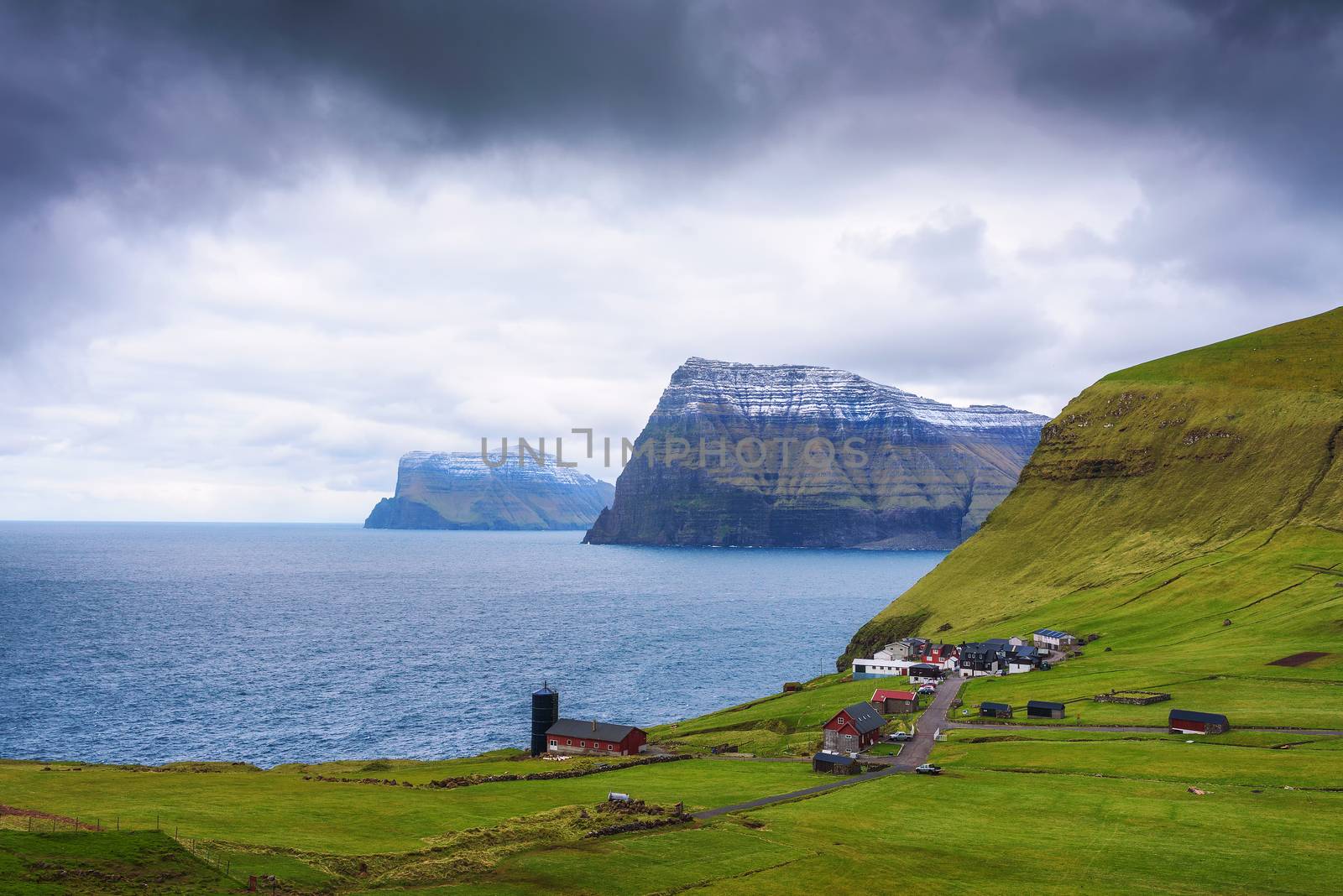 Village of Trollanes located on the island of Kalsoy in Faroe Islands with snow-capped mountains of Kunoy and Bordoy in the background