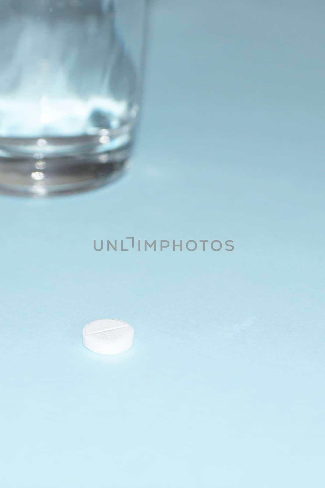 pill and glass of water on blue background close up by Annado