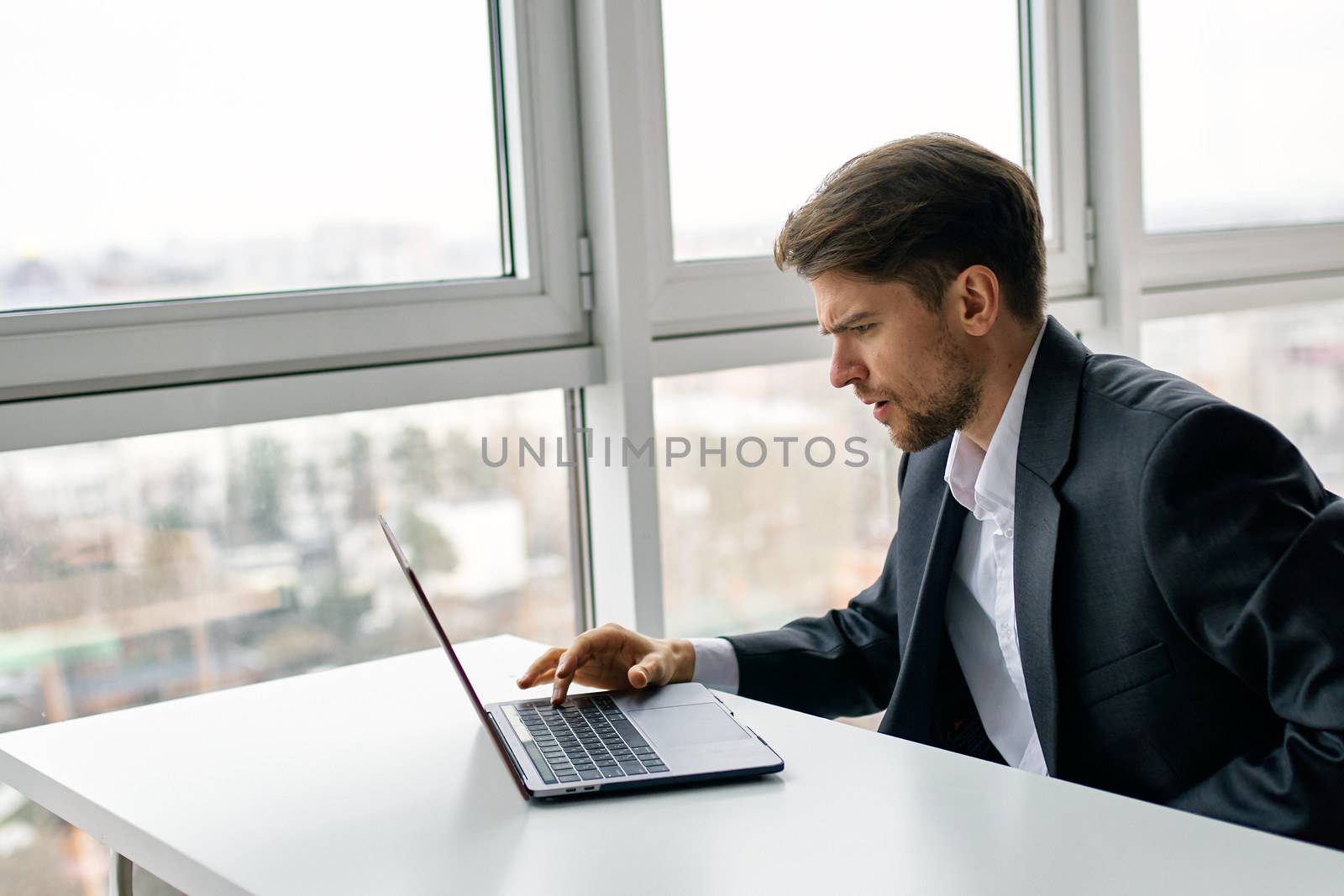 A man with a laptop is sitting at a table and is looking puzzled at the monitor