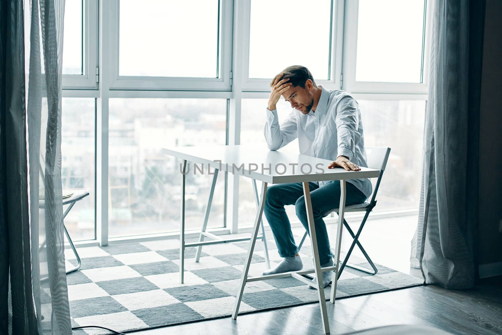 upset man sitting at a table indoors near a window