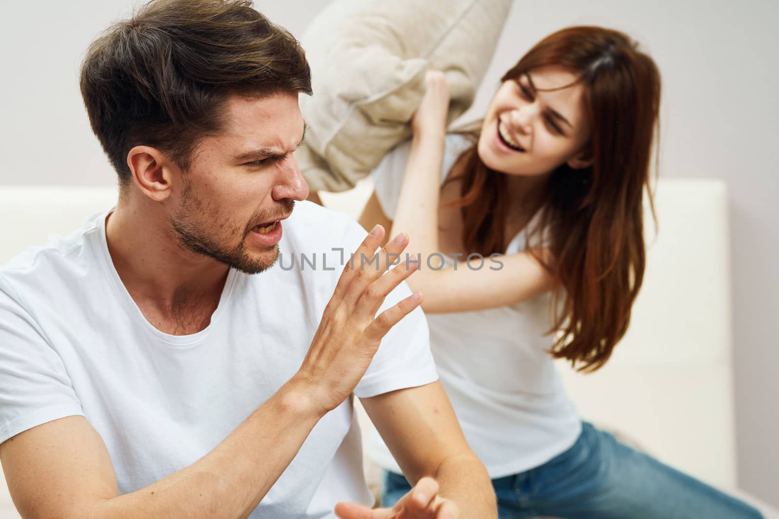 Happy man and woman fight pillows on the bed and indoors