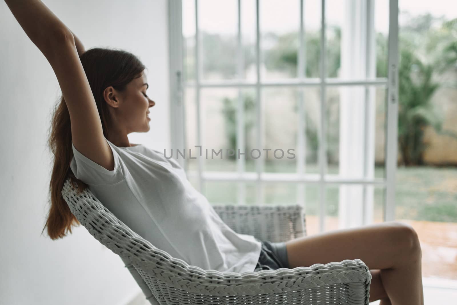 Happy girl near the window in an armchair with arms raised up