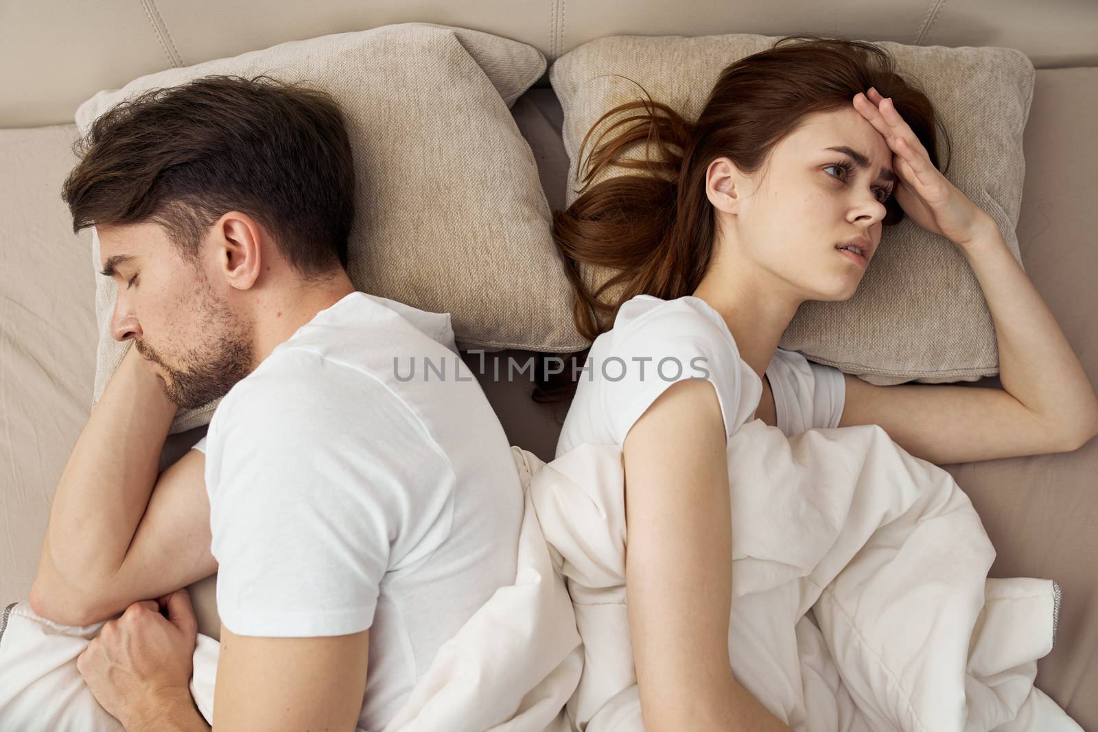 An upset woman lies in bed and the man next to her has problems in the family