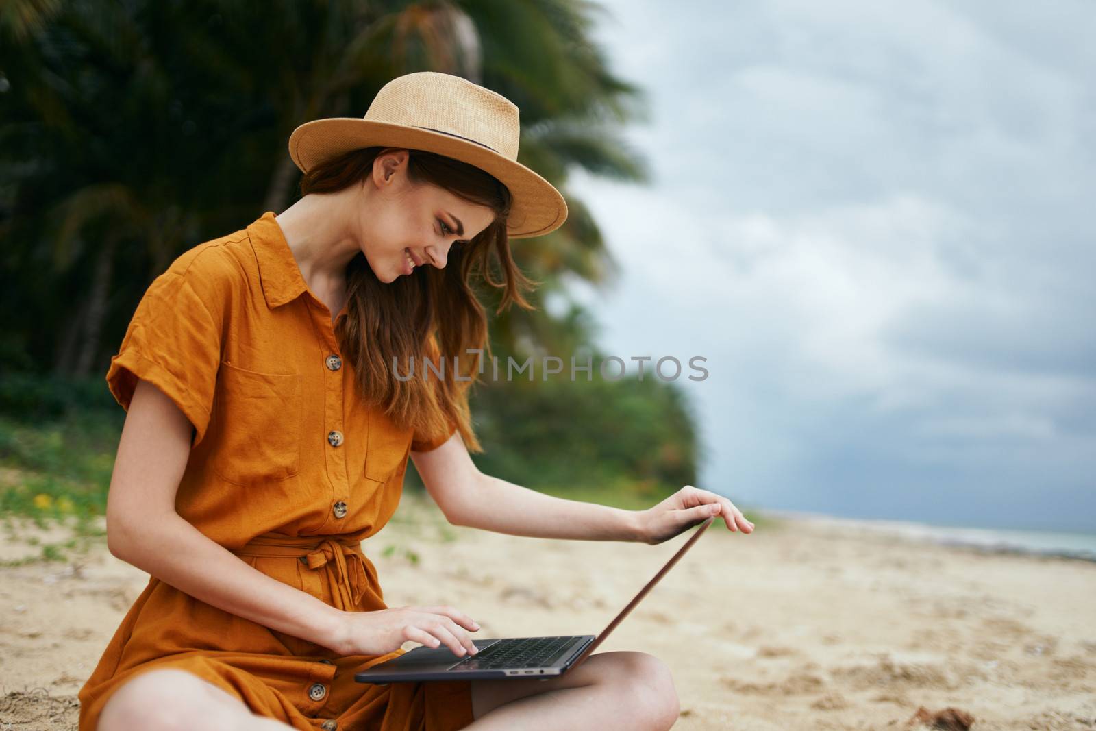 Beautiful woman with a laptop sits on the sand and works on nature