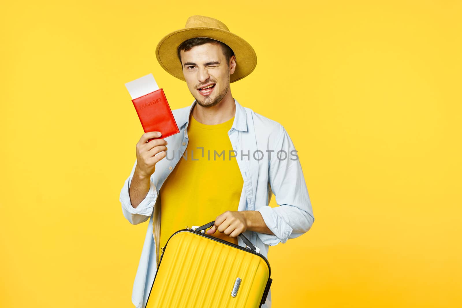 Happy traveler with a suitcase shows a passport to the camera and winks