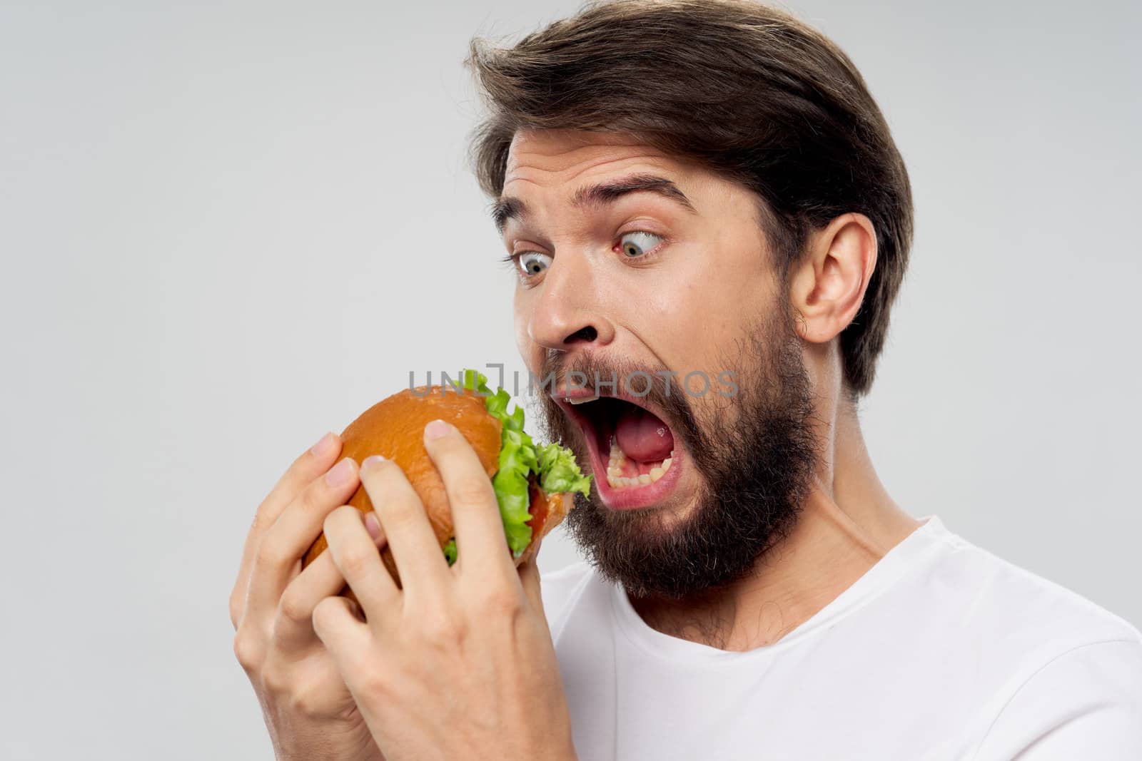 A hungry man with a huge hamburger opened his mouth wide on an isolated background