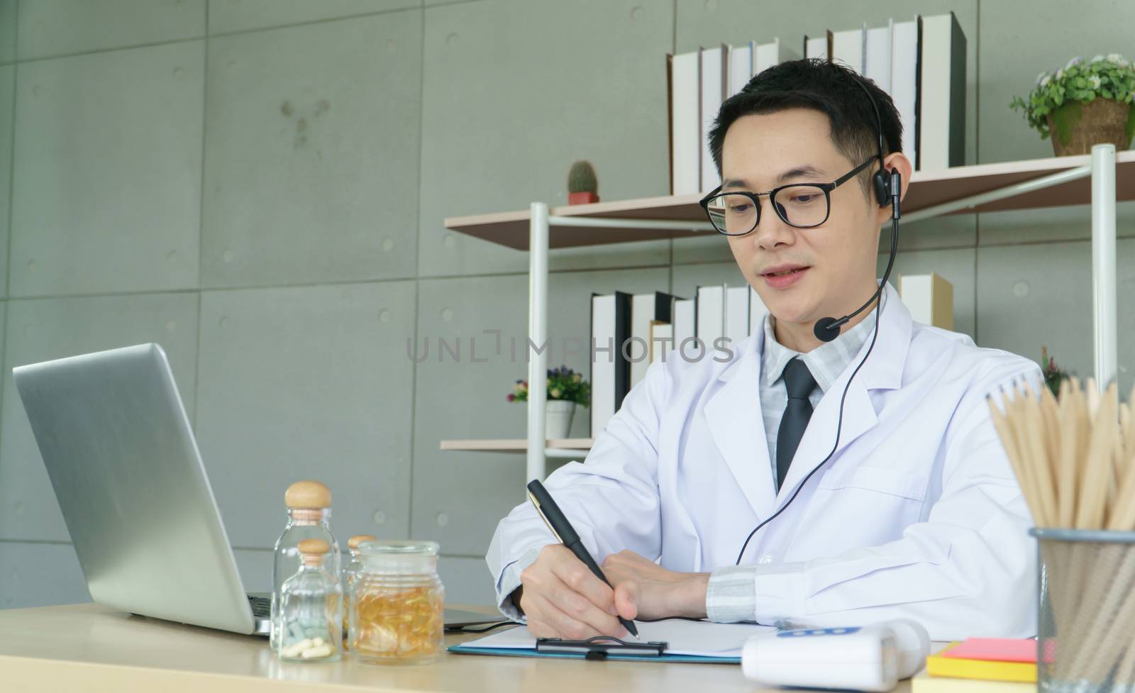 Asian male doctor is using a laptop computer to connect to the internet for online counseling. The medical profession, technology, communication, distance, and people concept