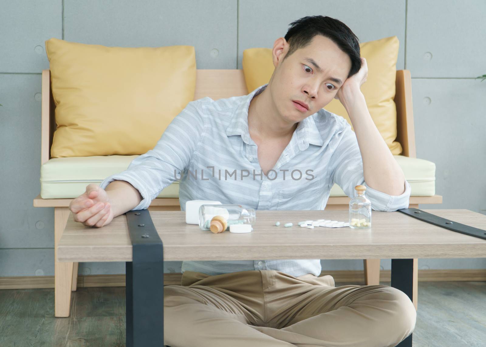 A young Asian man has a headache and Sick and stressed, he looked at the tablets that were eaten for healing and rehabilitation. As for advised by a medical professional