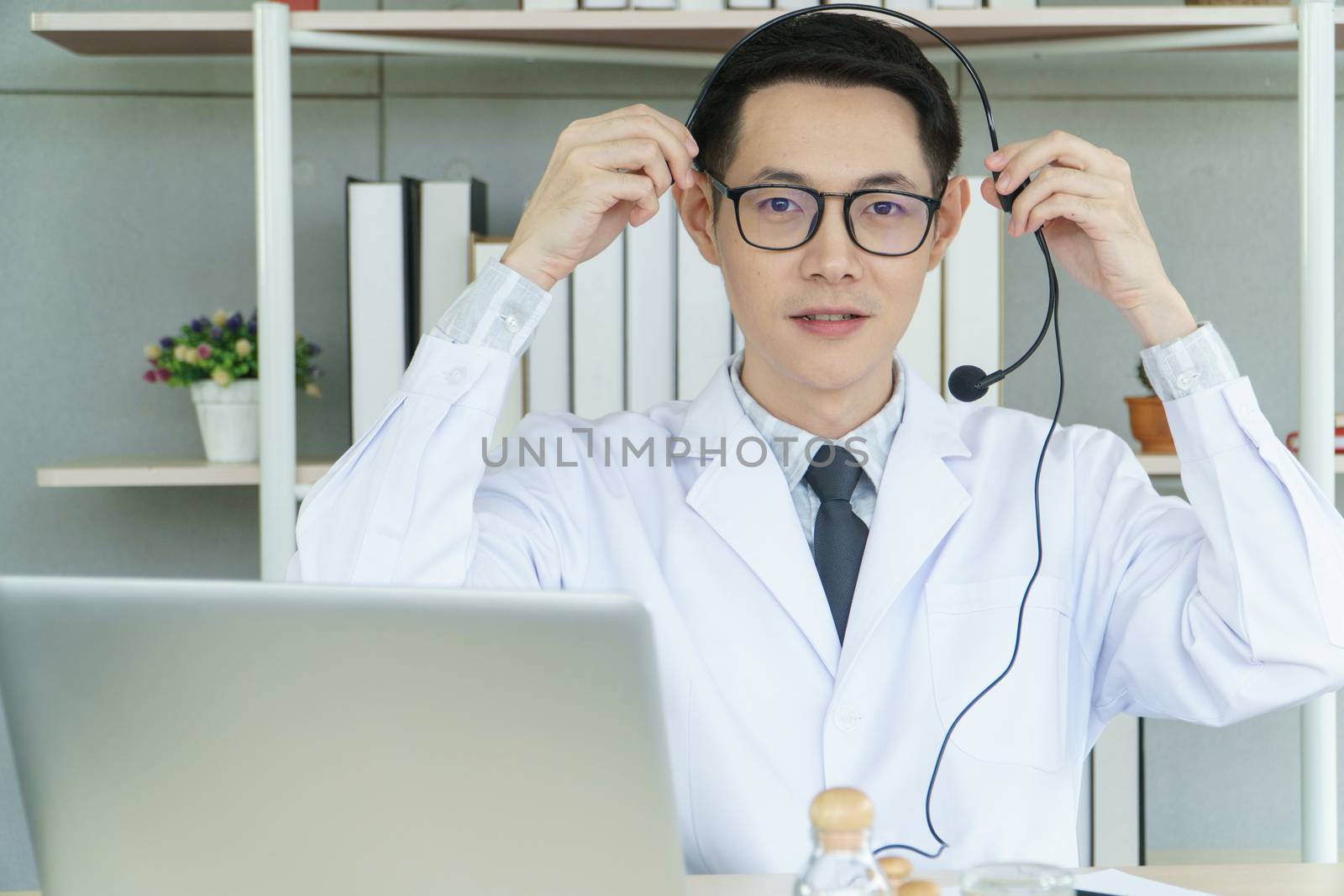 Asian male doctor is using a laptop computer to connect to the internet for online counseling. The medical profession, technology, communication, distance, and people concept