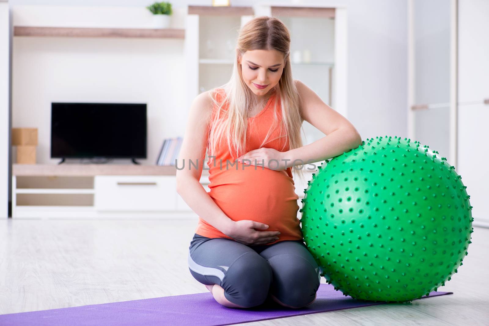 Young woman preparing for birth exercising at home by Elnur