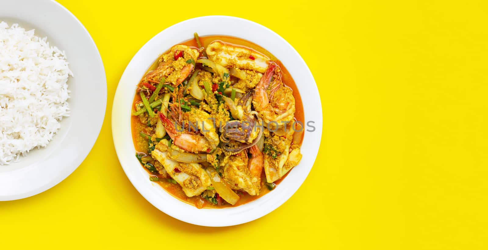 Fried seafood with curry powder with dish of rice on yellow background.