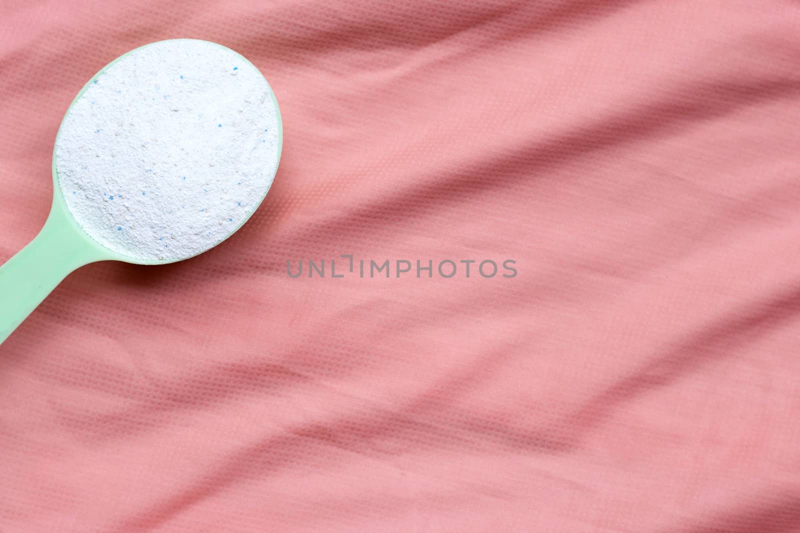 Detergent powder in measuring spoon on pink cloth. Laundry concept.