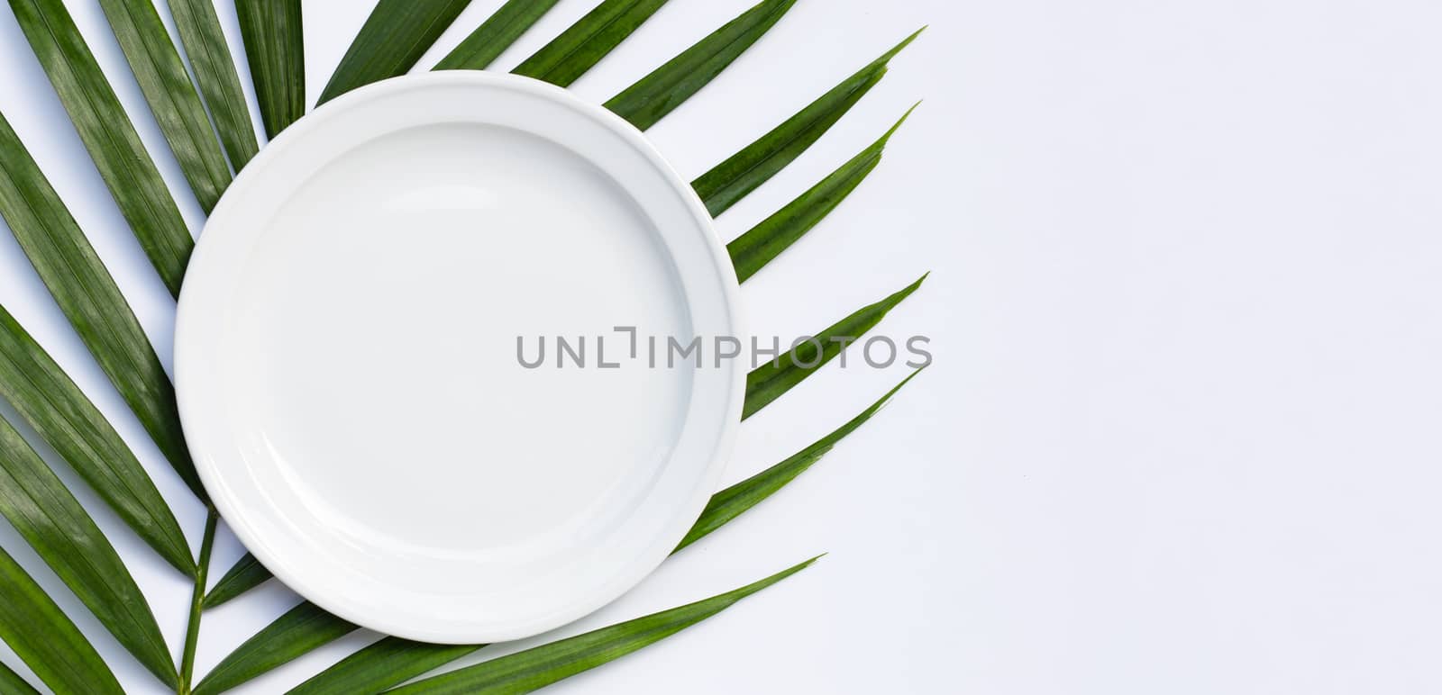 Empty white ceramic plate on tropical palm leaves on white background. Top view