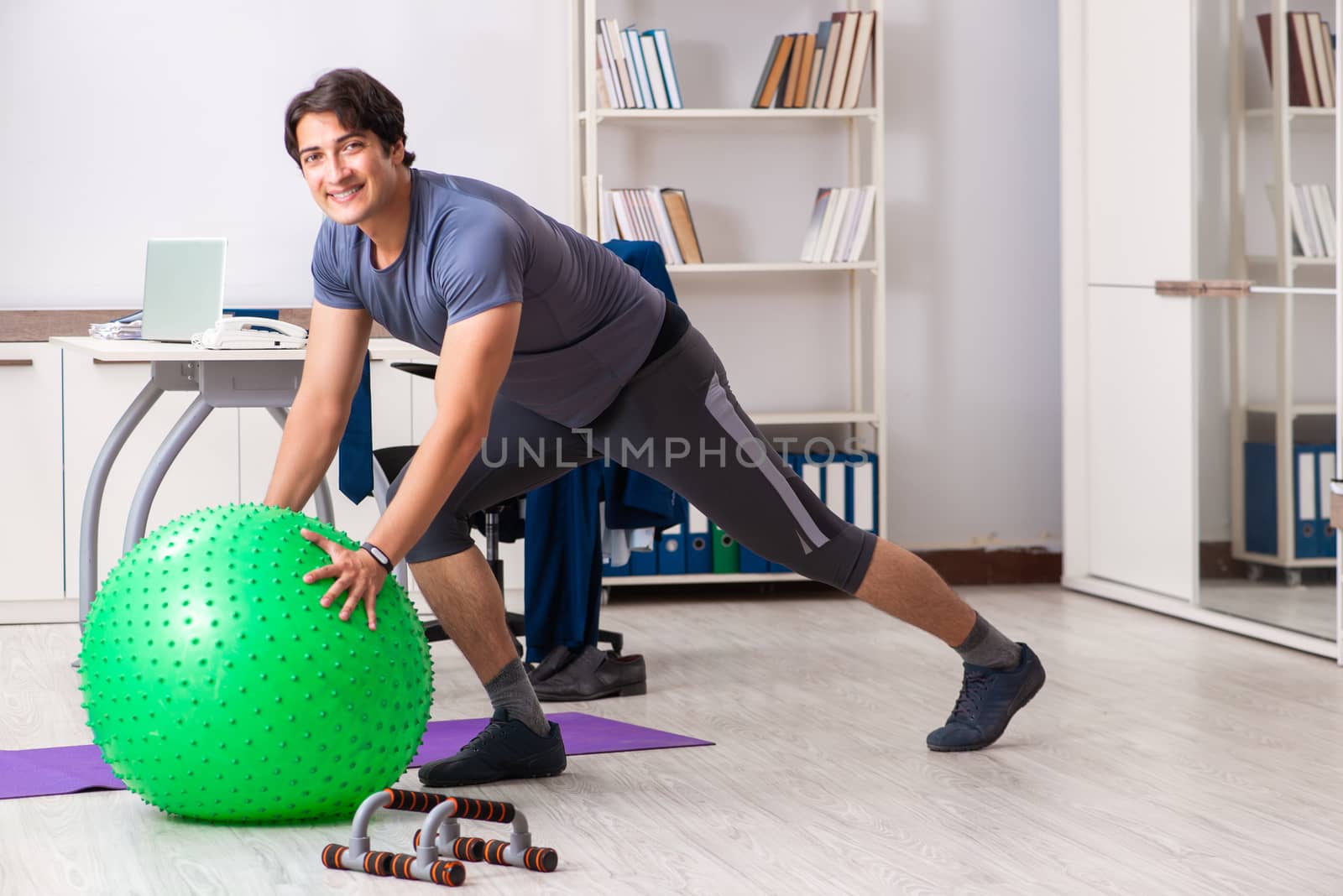 Young male employee exercising in the office by Elnur