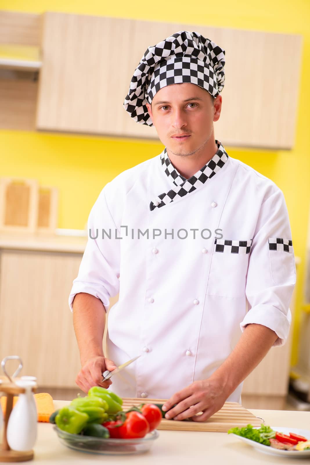 Young professional cook preparing salad at kitchen