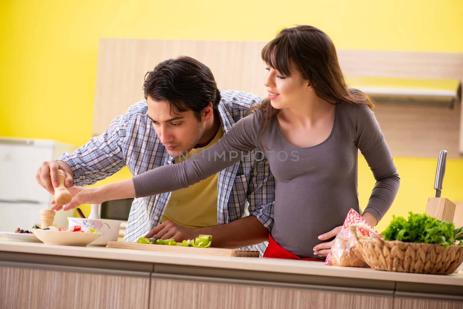 Man and pregnant woman preparing salad in kitchen 