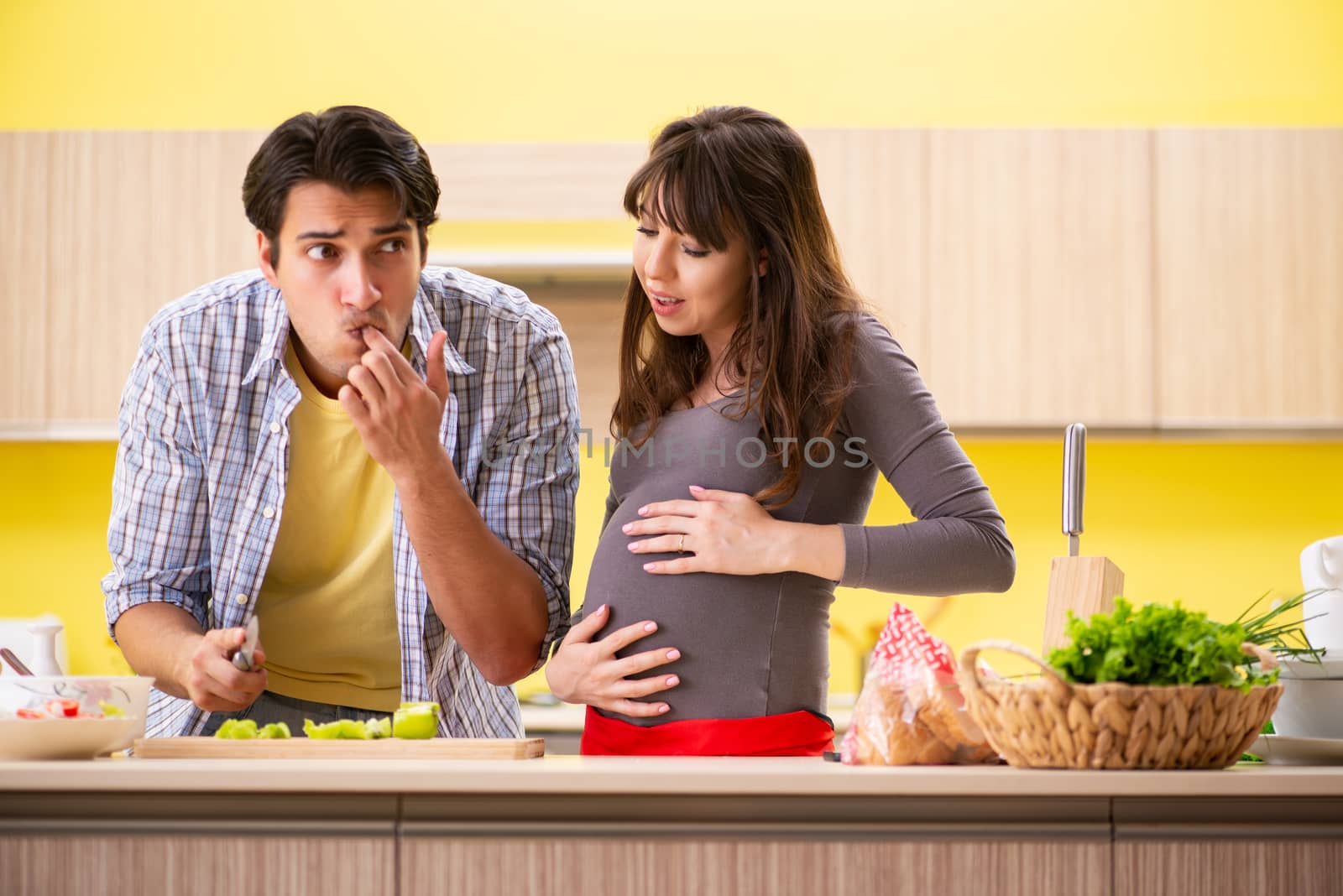 Man and pregnant woman preparing salad in kitchen 