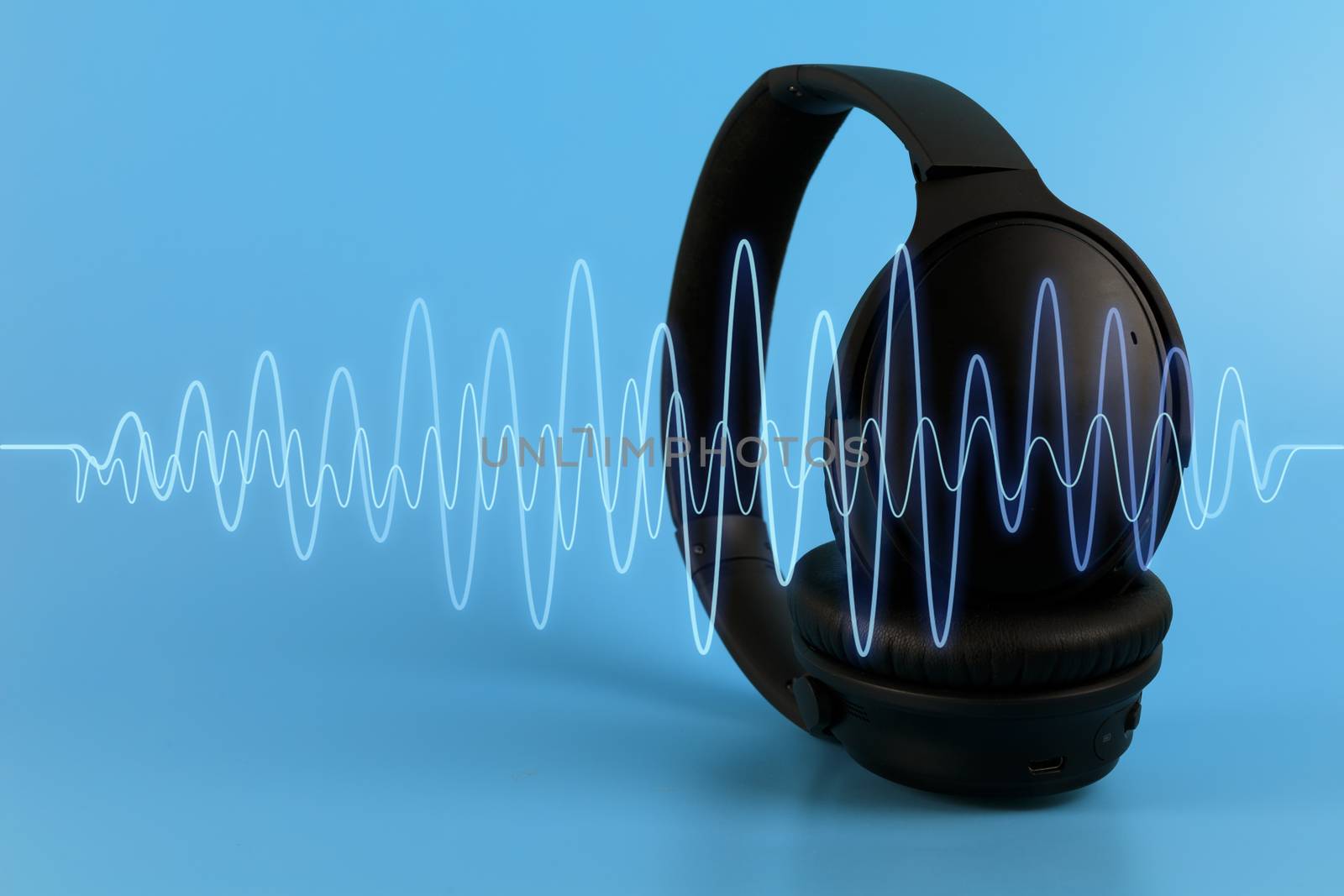 Black music headphones with blue sound wave on blue background.  by Satrinekarn