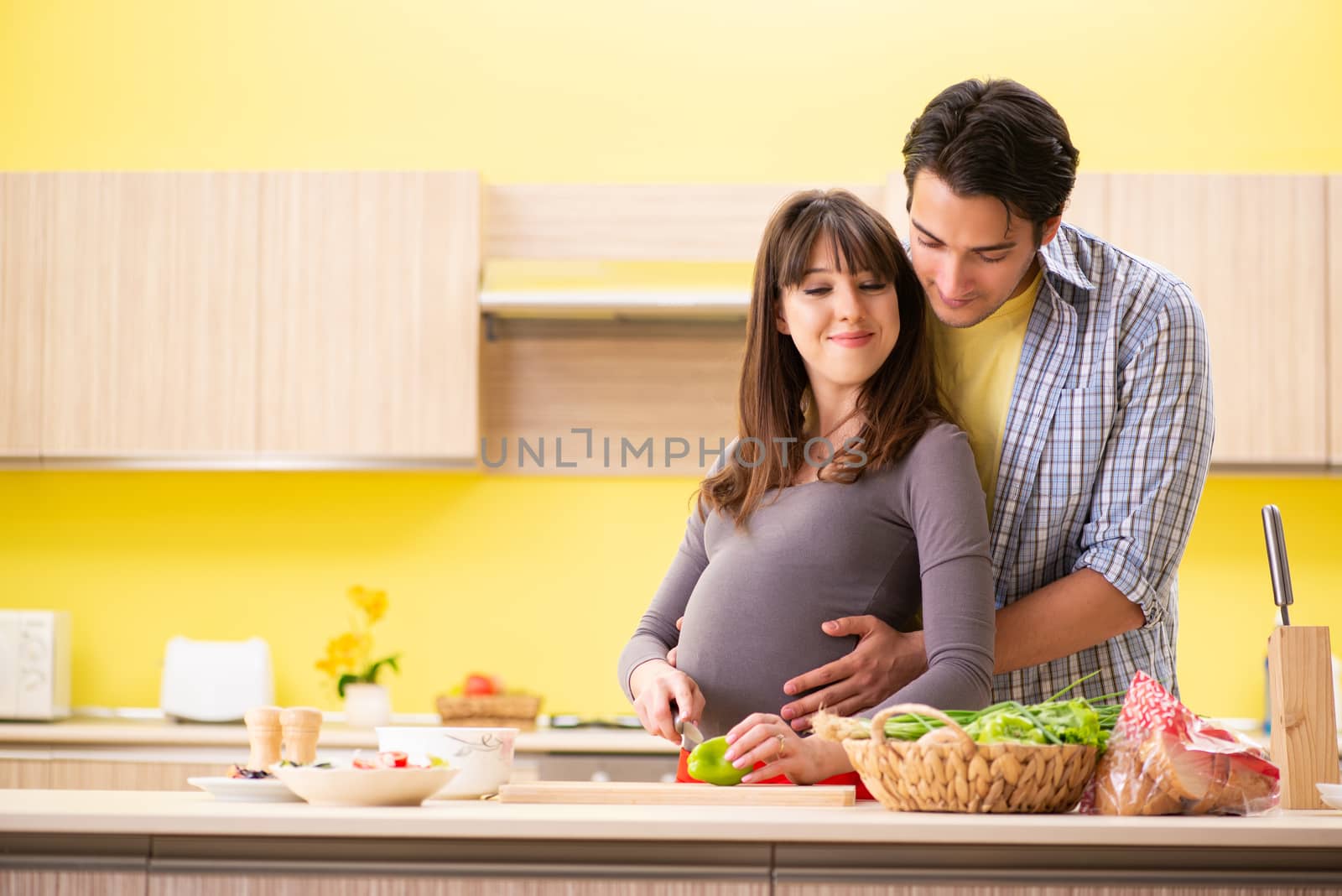 Man and pregnant woman preparing salad in kitchen 