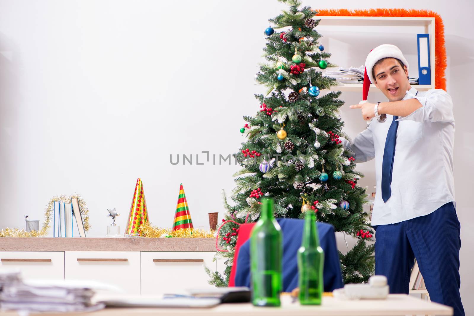 Young handsome employee celebrating Christmas at workplace 