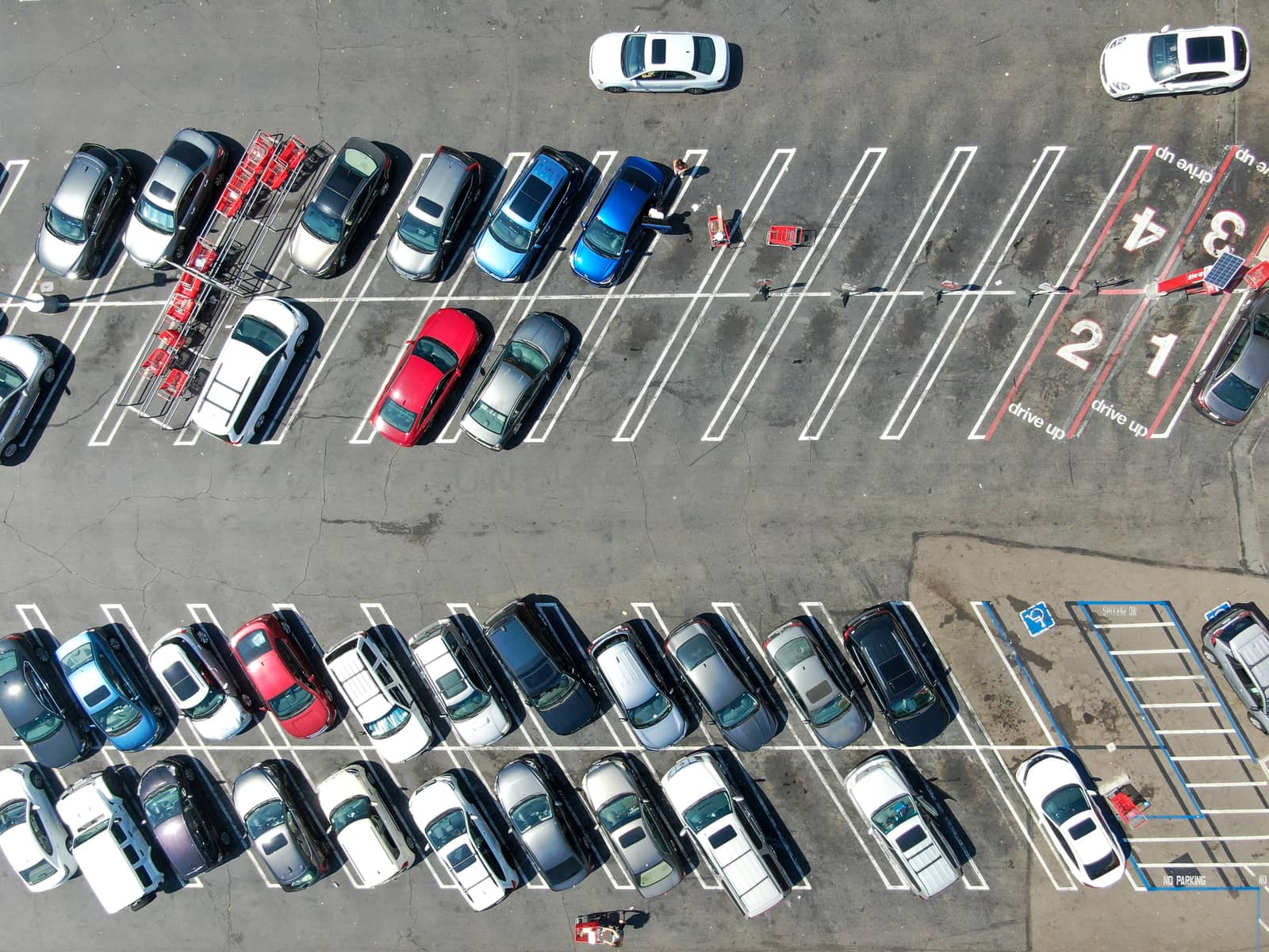 Aerial top view of parking lot at shopping mall with varieties of colored vehicles. People walking to their car and trying to park.